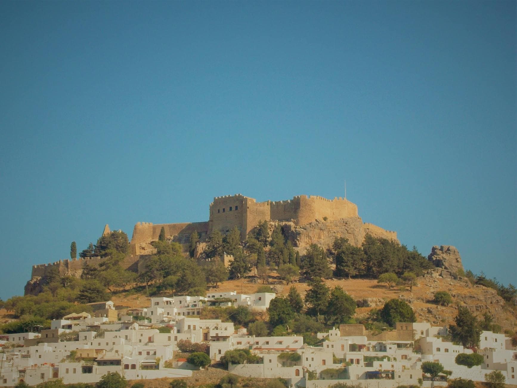 Scenic view of the Lindos Acropolis on a hill with a clear blue sky backdrop.