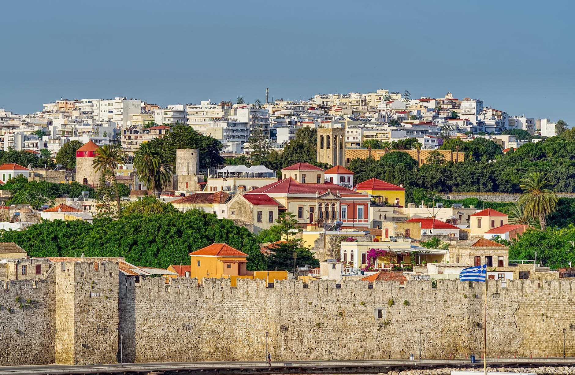 Explore the picturesque Rhodes Old Town with its colorful buildings and iconic medieval walls under a clear blue sky.