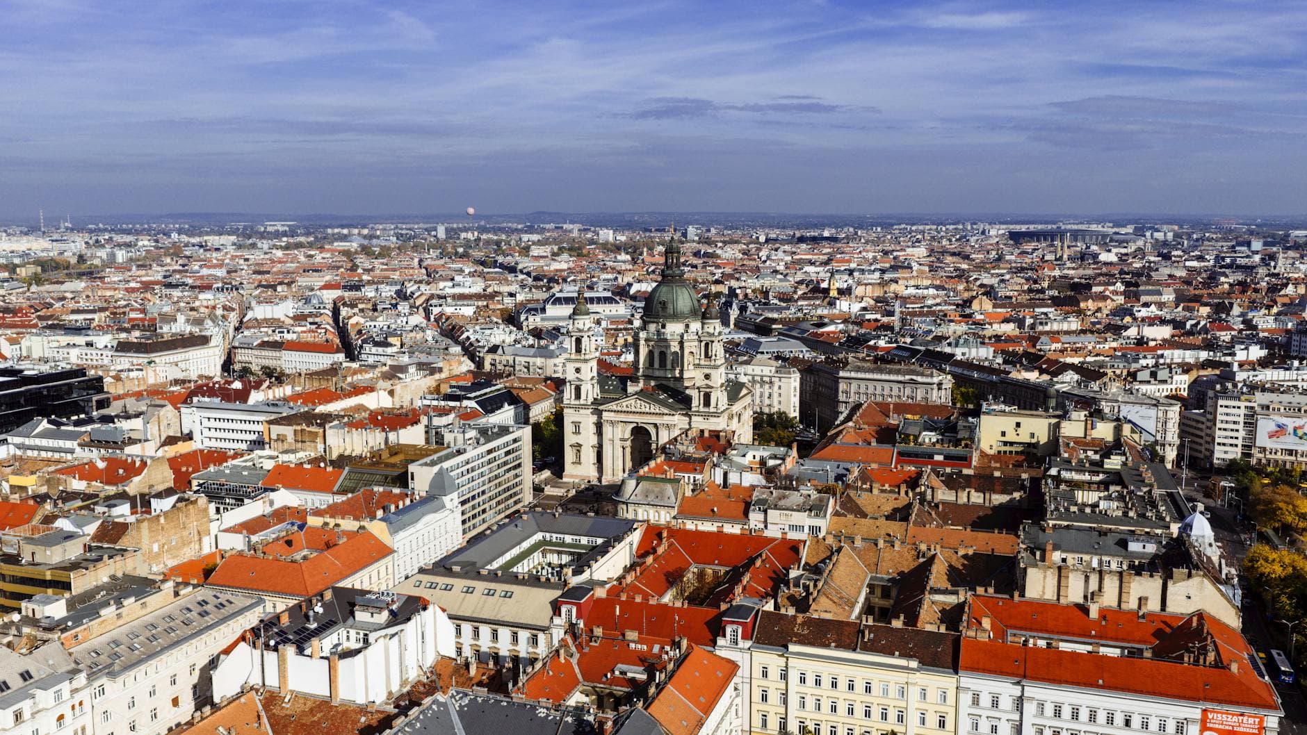 Stunning aerial shot of Budapest cityscape featuring St. Stephen's Basilica with orange roofs and blue sky.