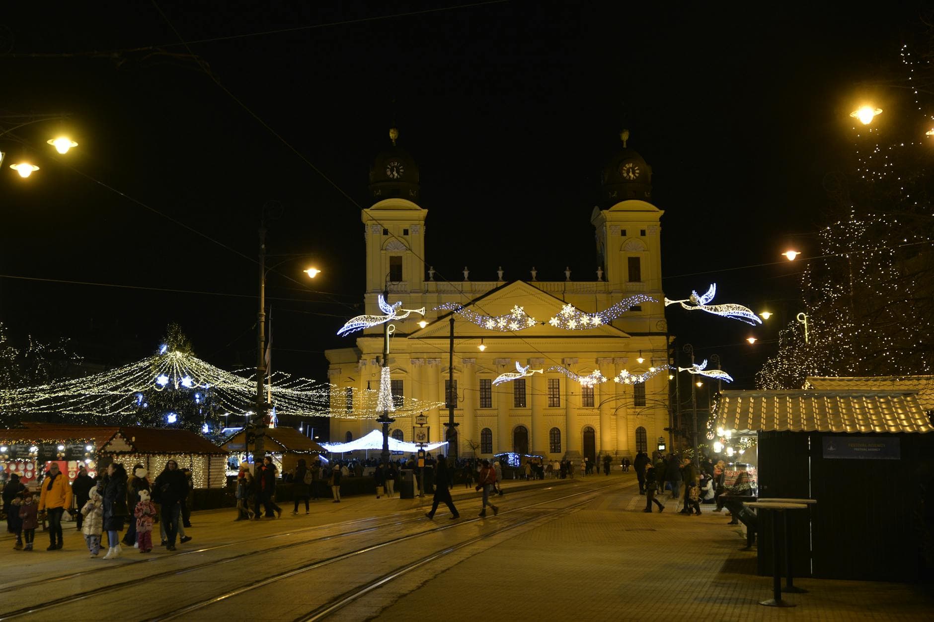 Night view of Debrecen Reformed Church adorned with festive Christmas lights and bustling holiday market.