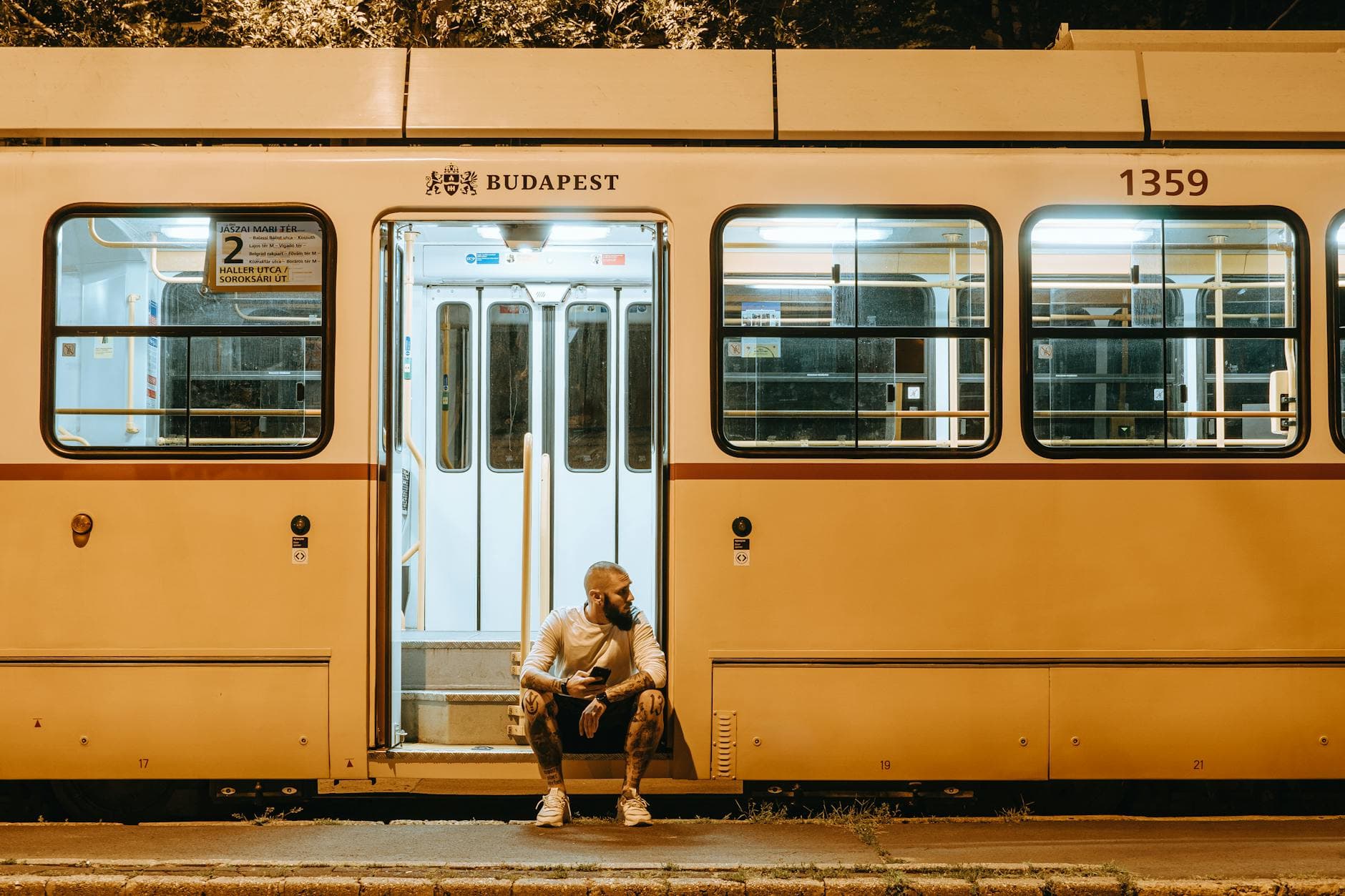 A man sits on the steps of a Budapest tram during nighttime, creating a serene urban mood.