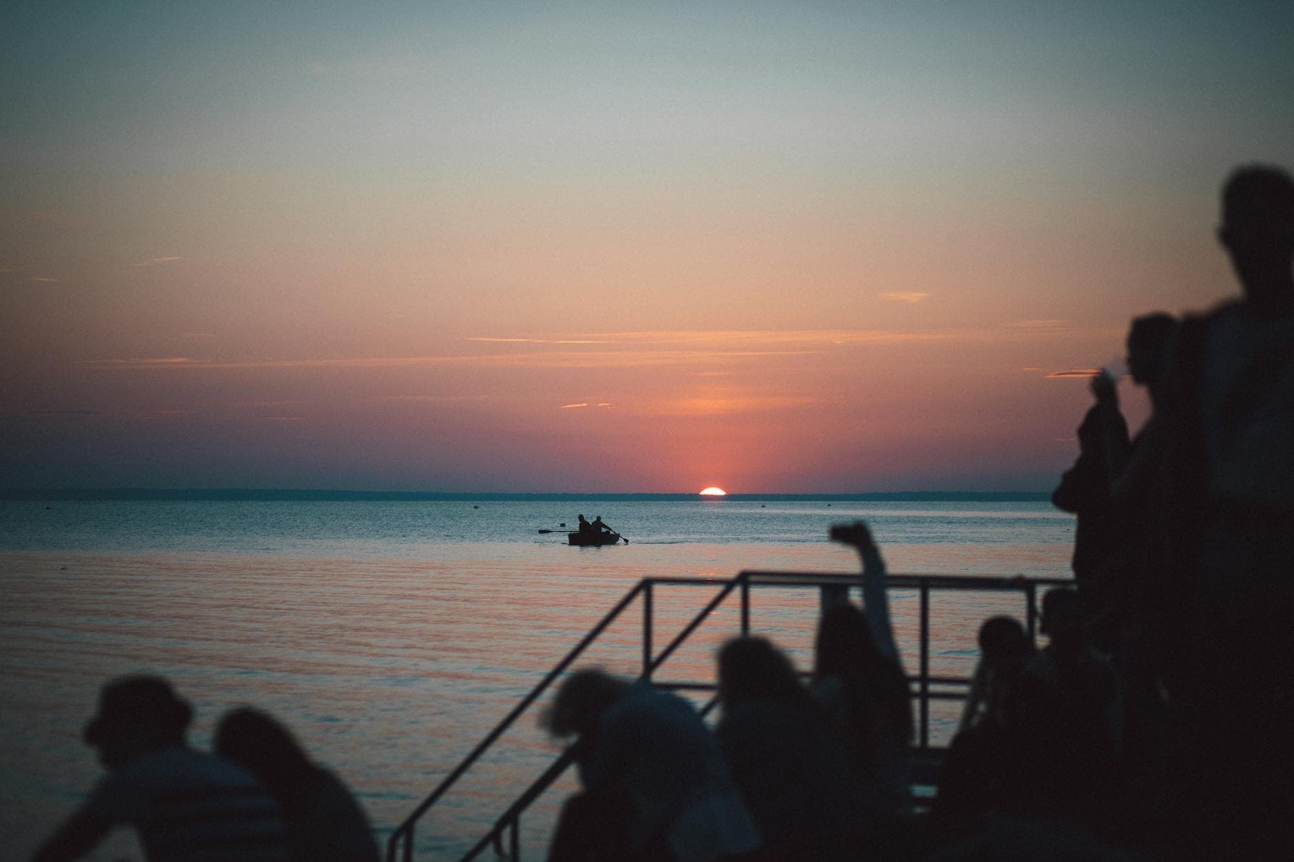 Peaceful sunset over Lake Balaton with silhouettes of people and boats, Hungary.
