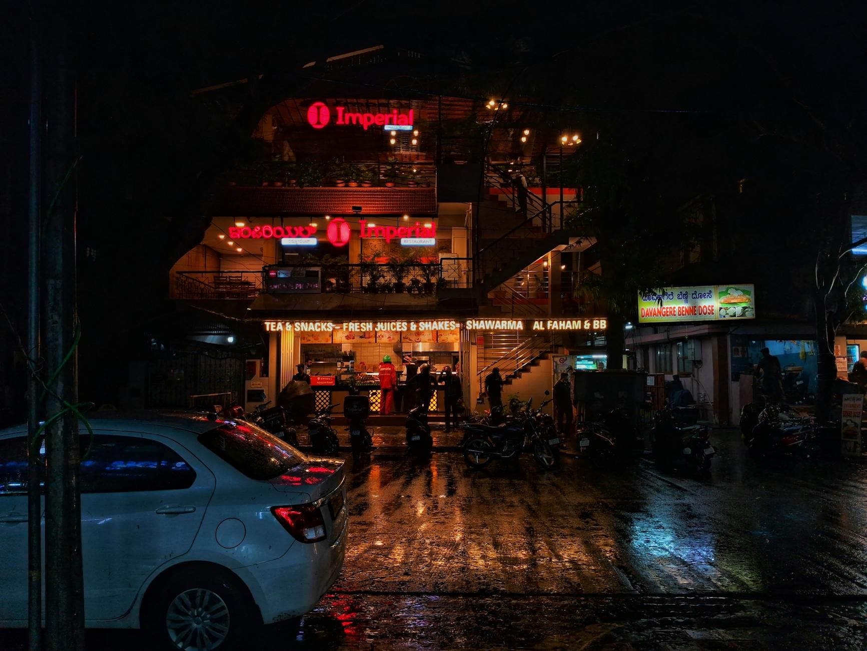 Rainy night street scene with cafes in Koramangala, India, capturing vibrant urban life.