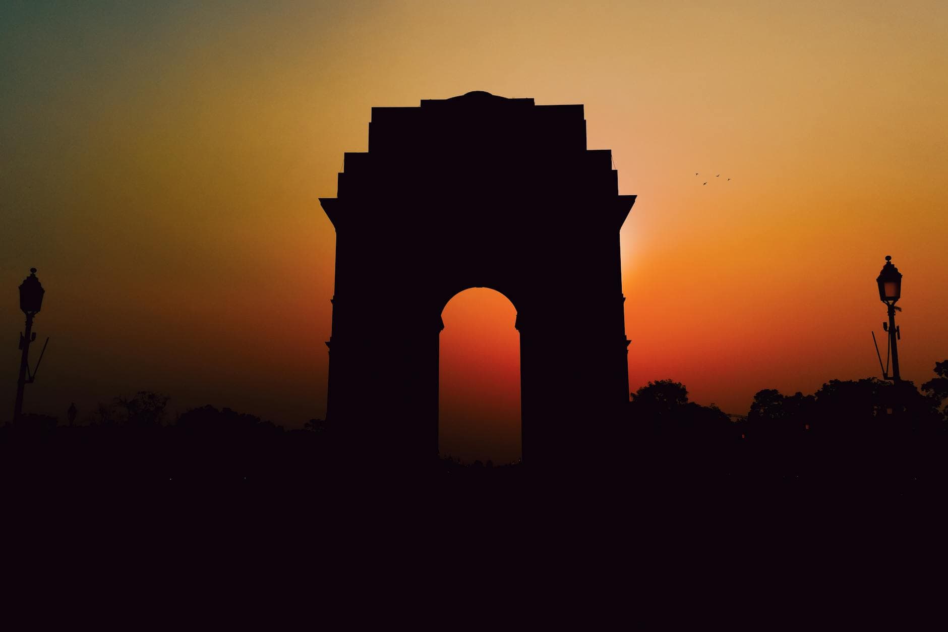 Silhouette of India Gate against a vibrant sunset in New Delhi, India, highlighting its iconic structure.