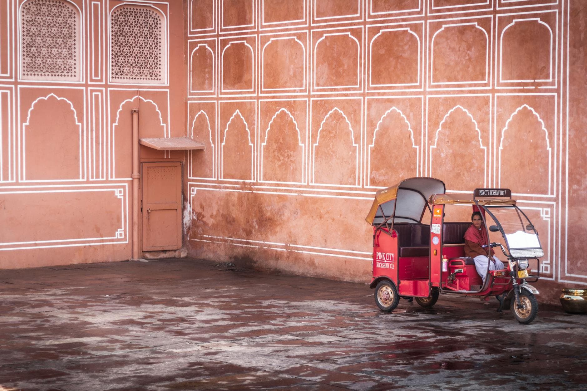 A woman in a tuk tuk against Jaipur's iconic pink architecture, Rajasthan, India.