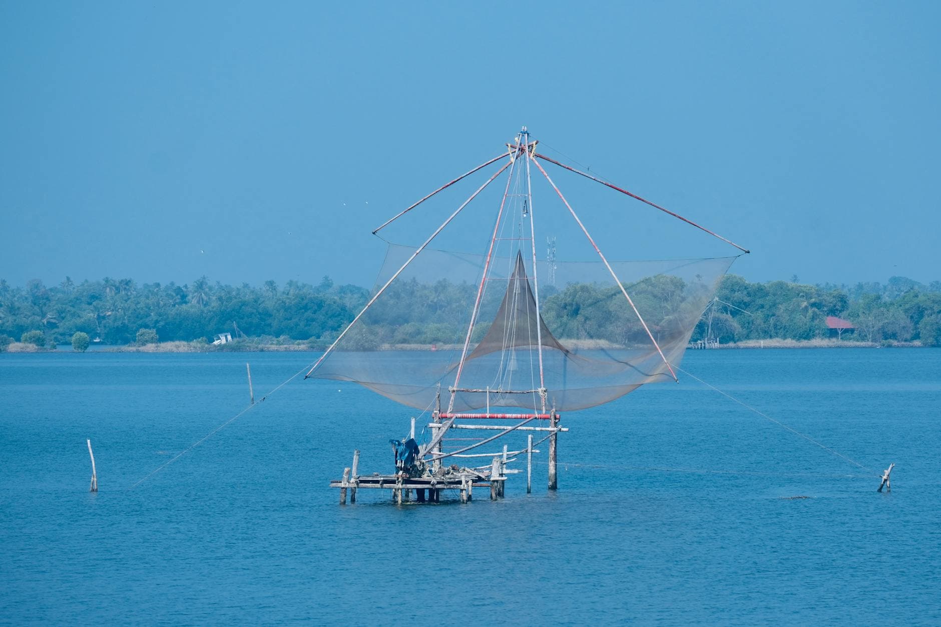 A picturesque view of a large Chinese fishing net on a tranquil coastline under a blue sky.