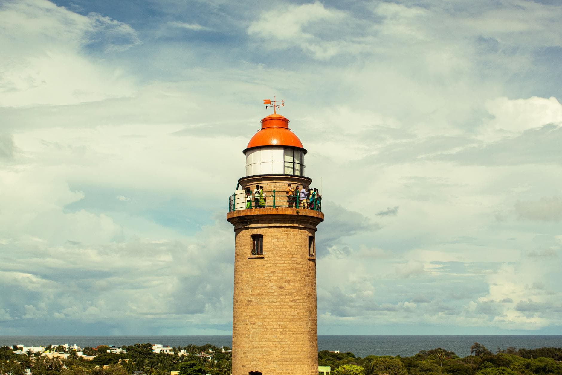 A scenic lighthouse with visitors atop, set against the vast Indian Ocean and blue sky.