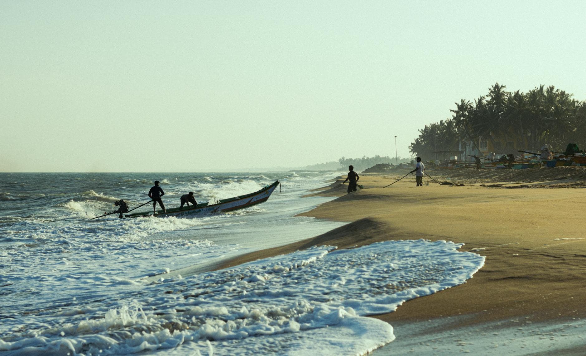 Fishermen set sail from a sandy beach in Puducherry, India, during a tranquil sunset.
