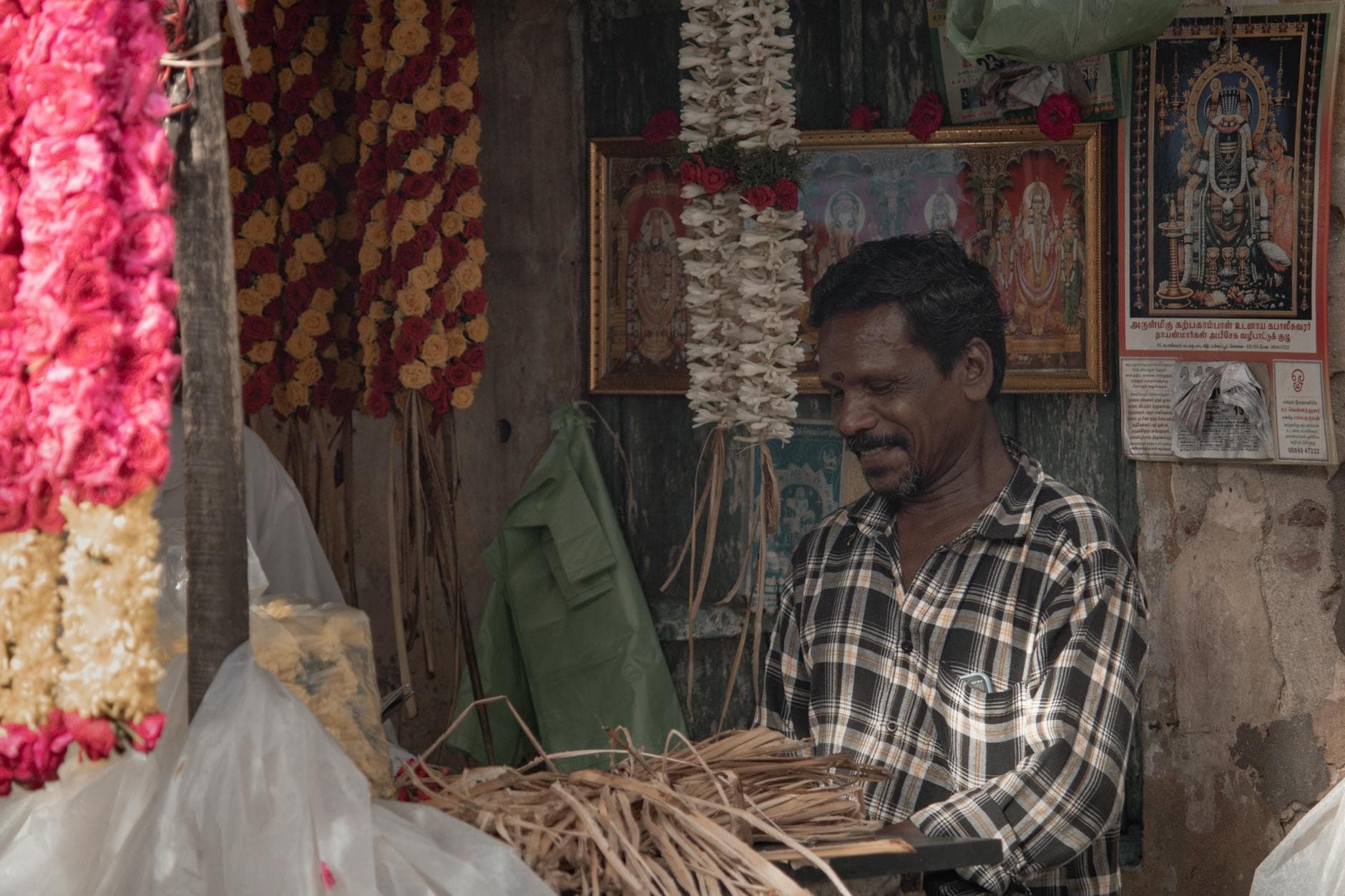A local flower vendor in Puducherry creates garlands amidst vibrant blossoms, showcasing Indian culture.