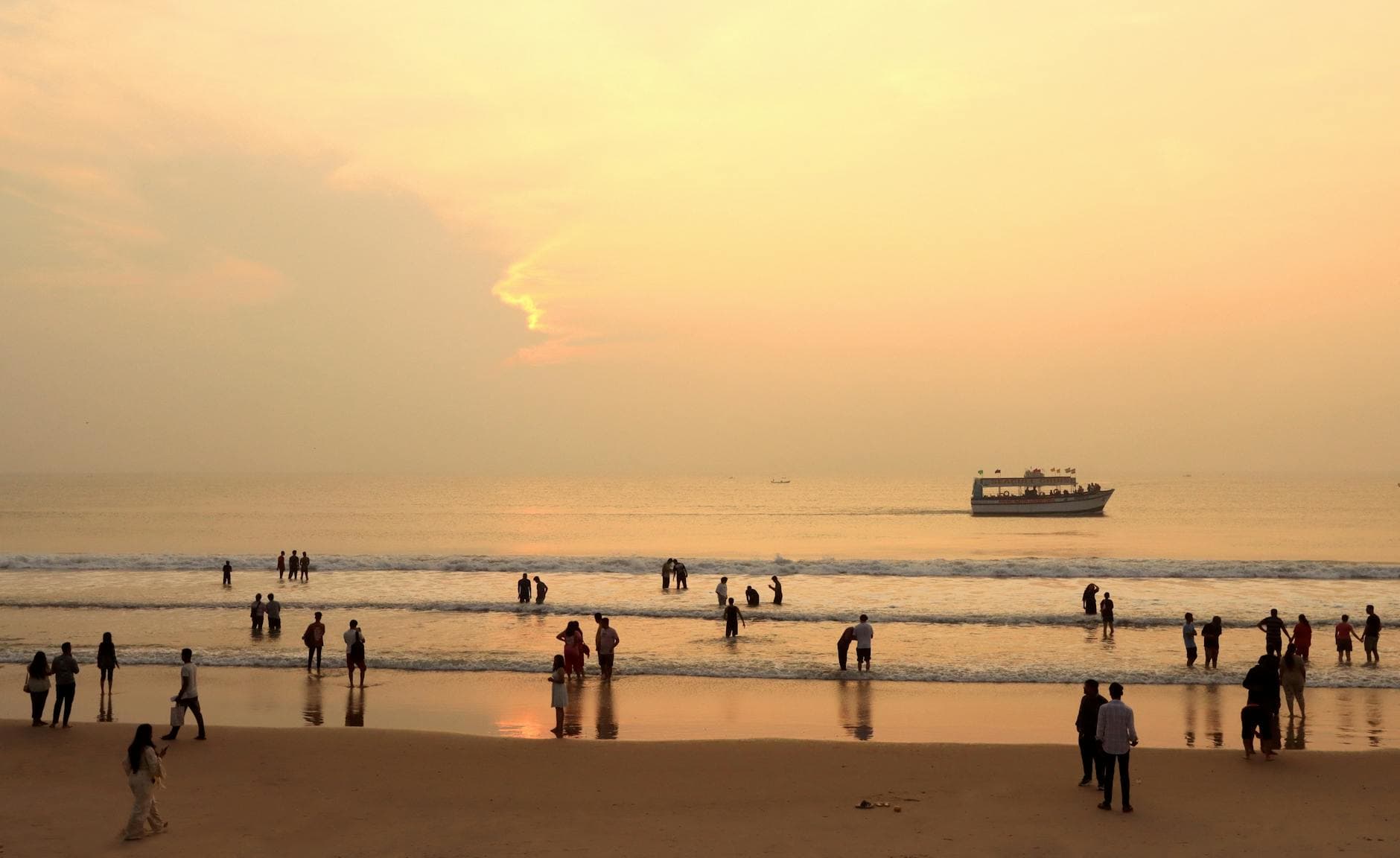 A serene beach scene in Pondicherry, India, at sunset with people enjoying the shoreline and a boat in the distance.