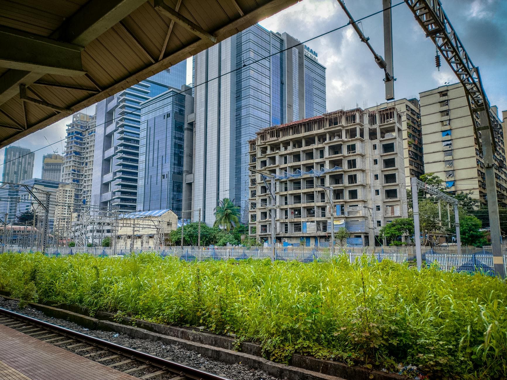 Modern skyscrapers in Mumbai viewed from a railway platform with lush greenery in the foreground.