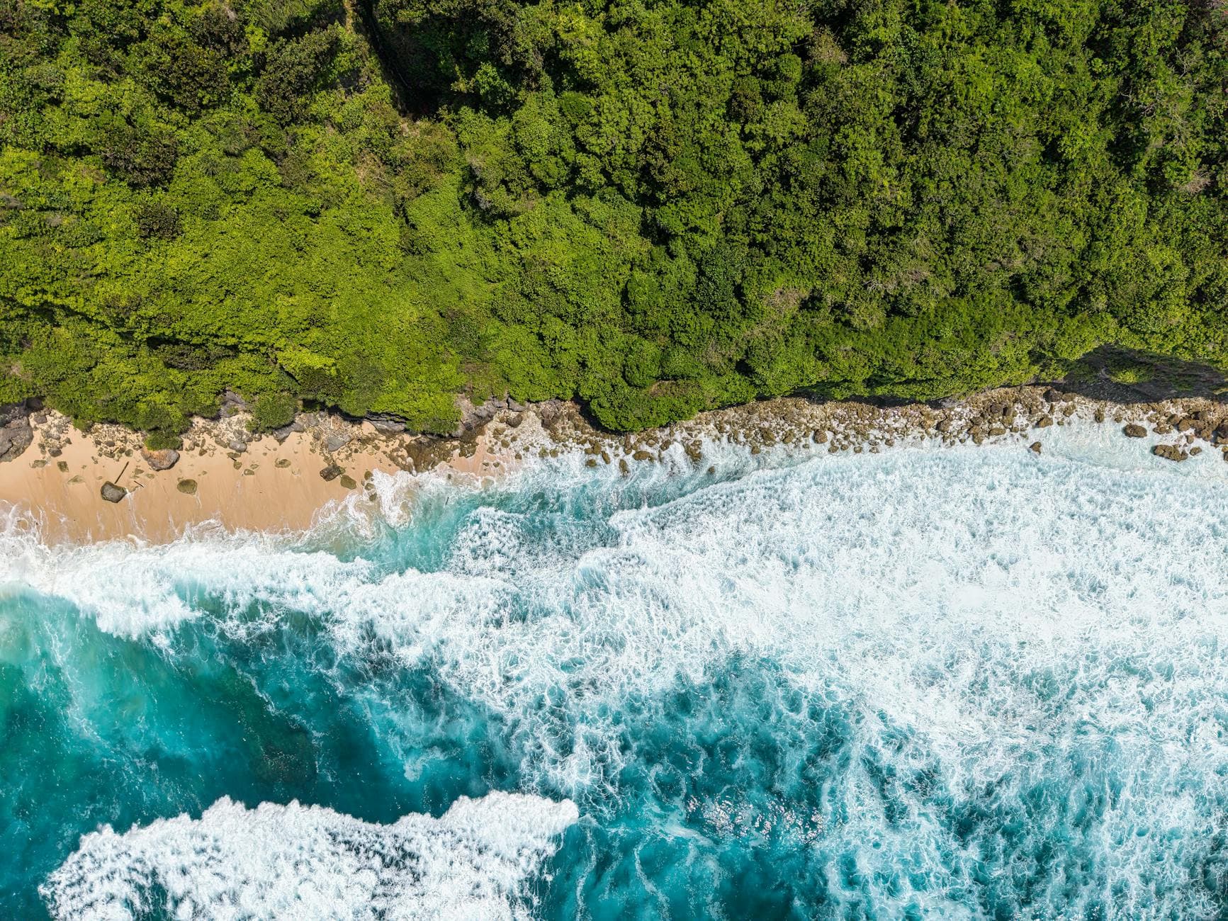 Stunning aerial view of Bali's coastline, vibrant ocean and lush greenery.