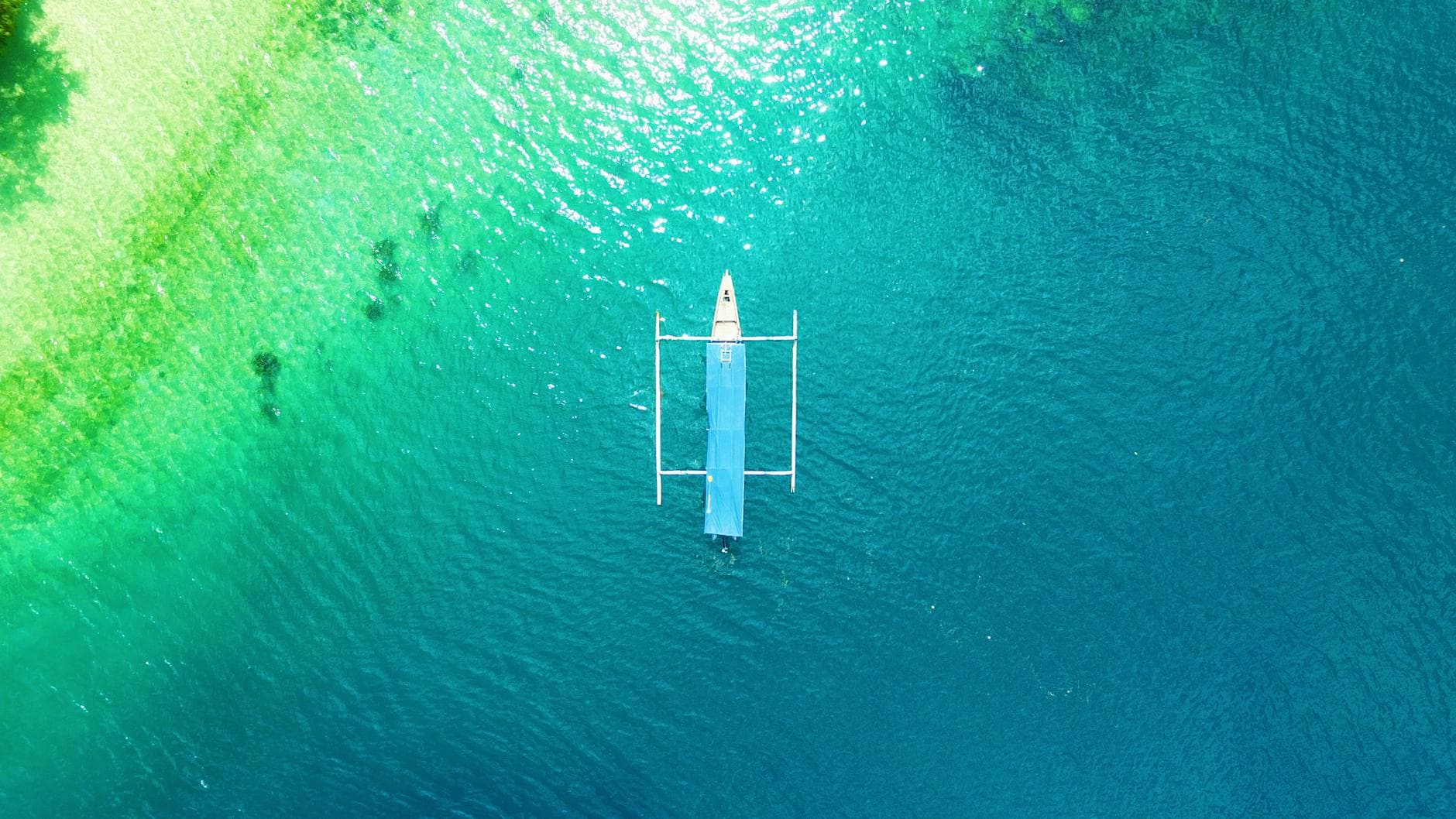 A drone capture of a boat floating on the vibrant turquoise waters of Lombok, Indonesia.