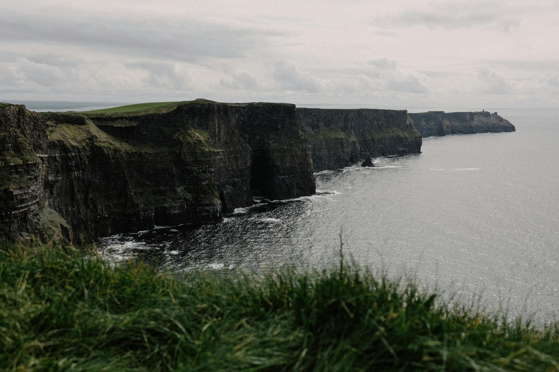 View of Ireland's iconic Cliffs of Moher with lush greenery and the Atlantic Ocean under cloudy skies.