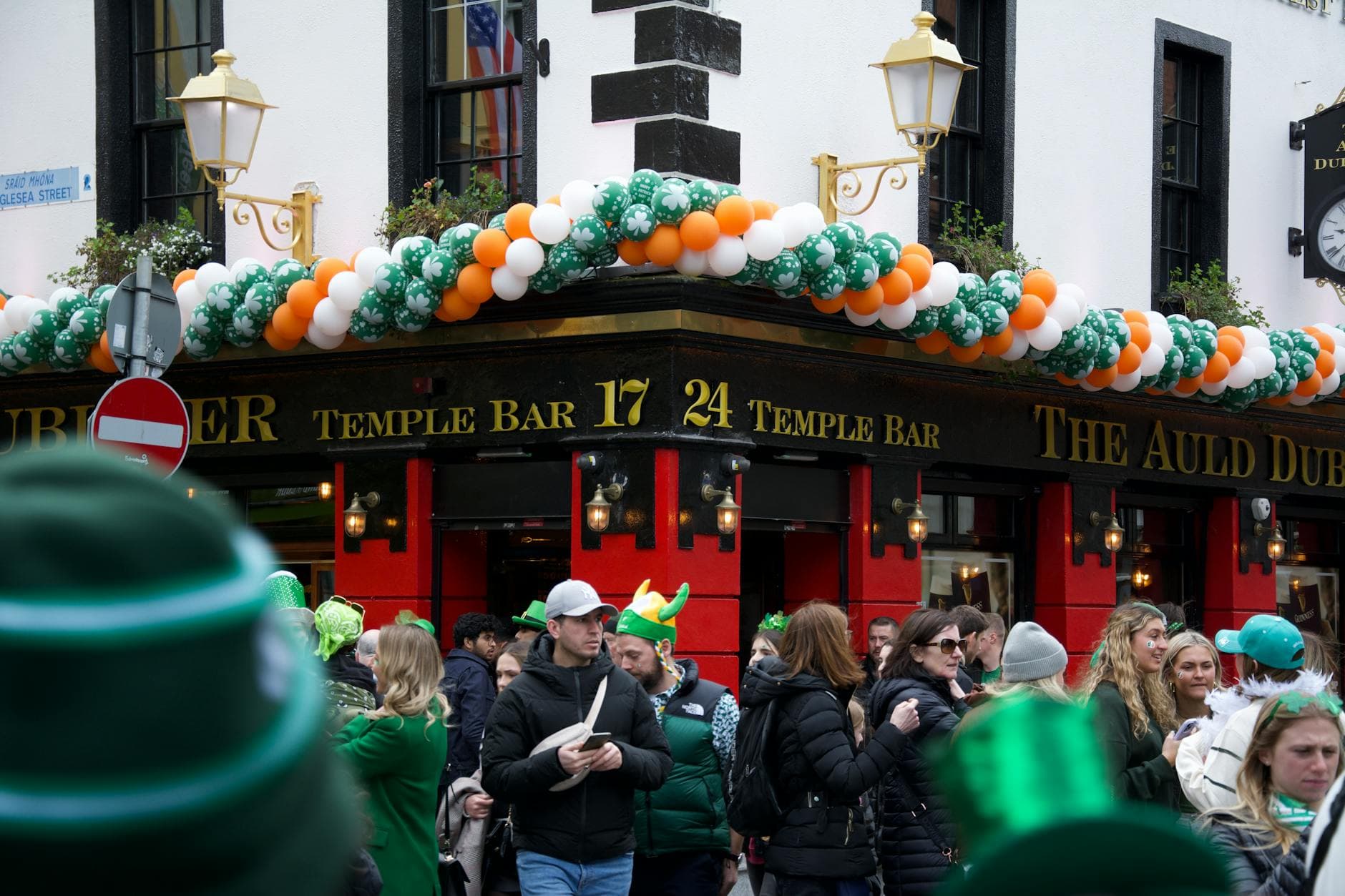 Festive crowd outside Temple Bar in Dublin during St. Patrick's Day with green decorations.