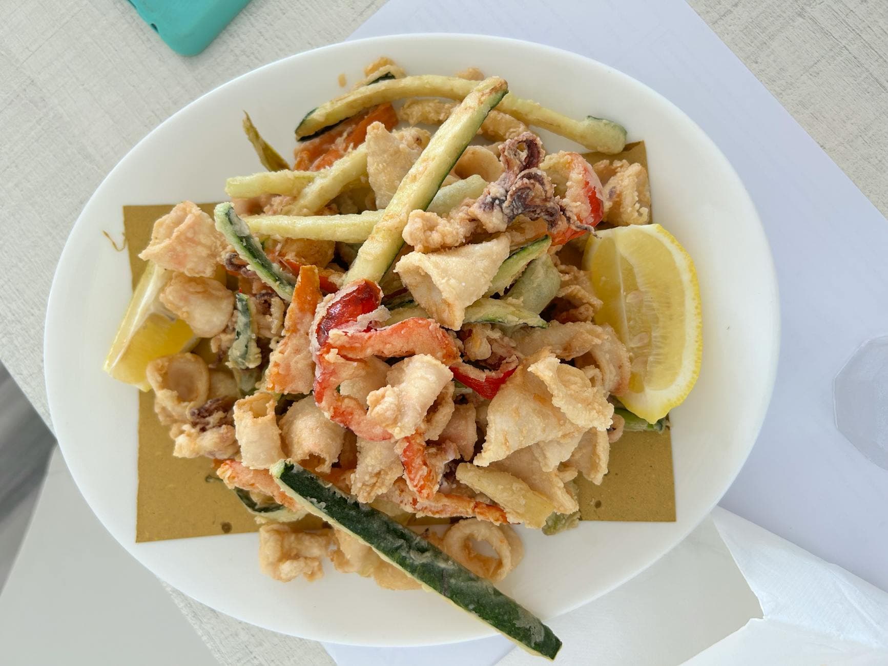 Delicious mixed fried seafood with zucchini and lemon on a white plate.