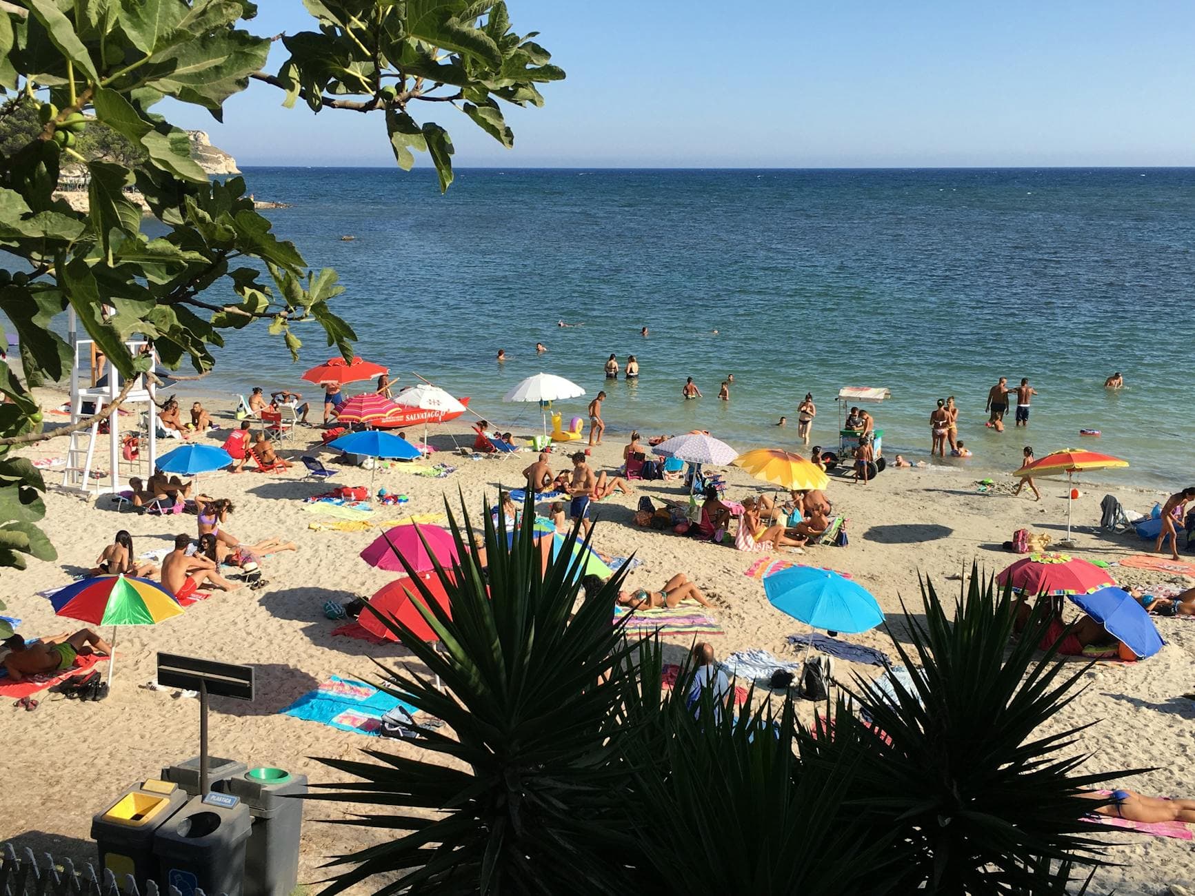 Lively seaside scene with sunbathers and colorful umbrellas on Poetto Beach, Sardinia.