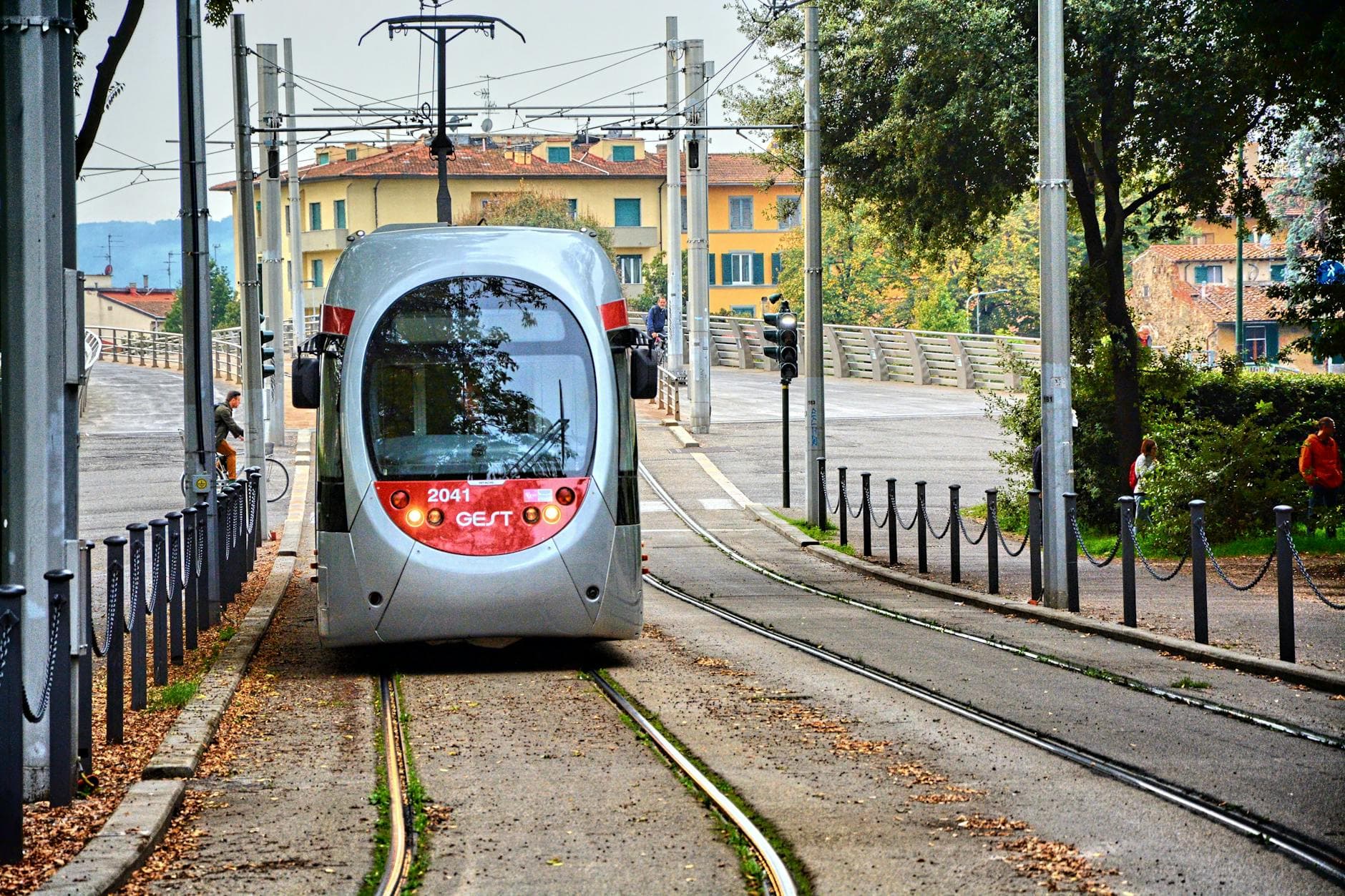 A sleek tram travels through a charming European town surrounded by trees and buildings.