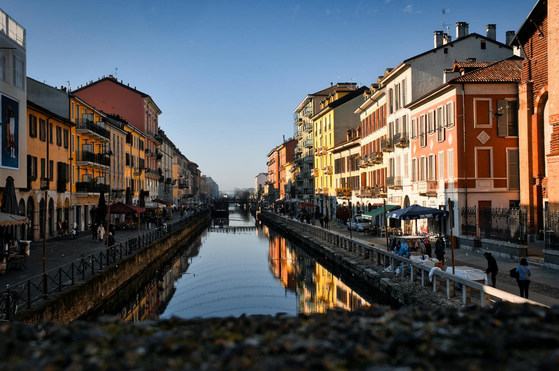 Charming scene of outdoor cafes and colorful buildings lining a canal in Milan's Navigli District.