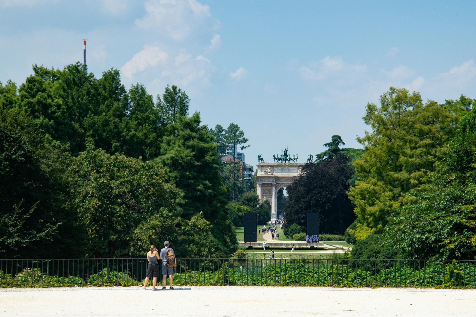 People enjoying a sunny day at Sempione Park with the iconic Arch of Peace in Milan.
