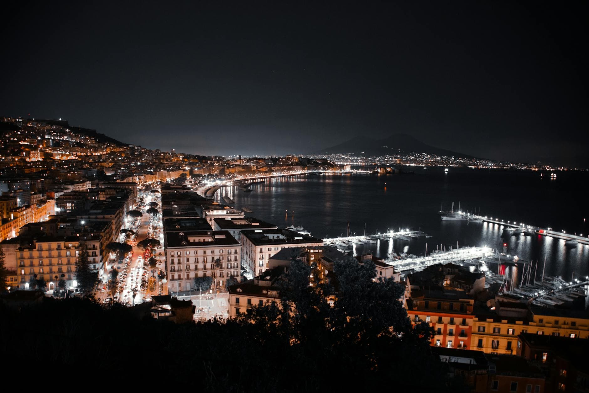 A captivating nighttime aerial view of Naples' coastline featuring vibrant city lights and serene water.