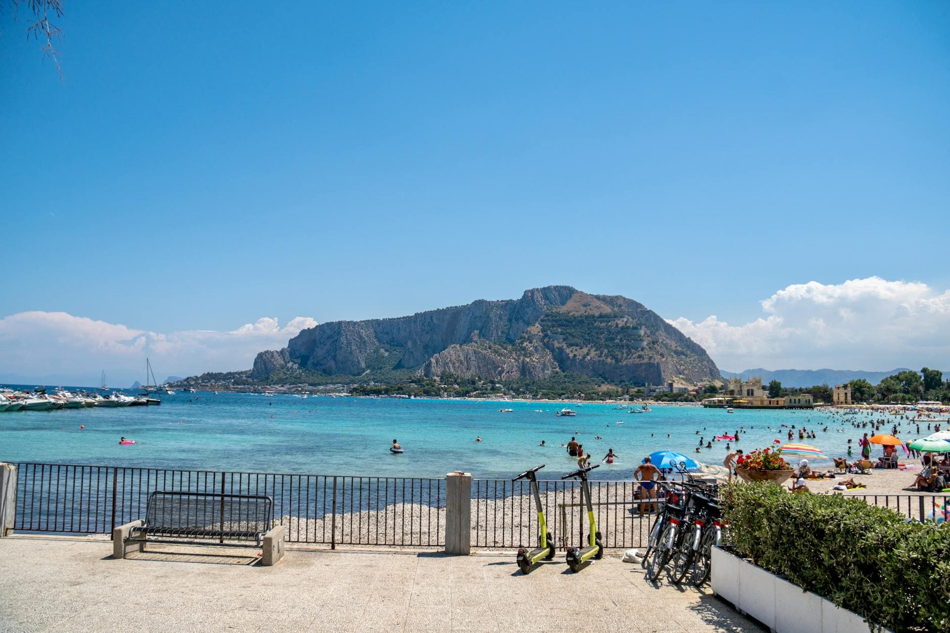 A sunny day at Mondello Beach, Sicily, featuring clear waters, mountains, and leisure activities.