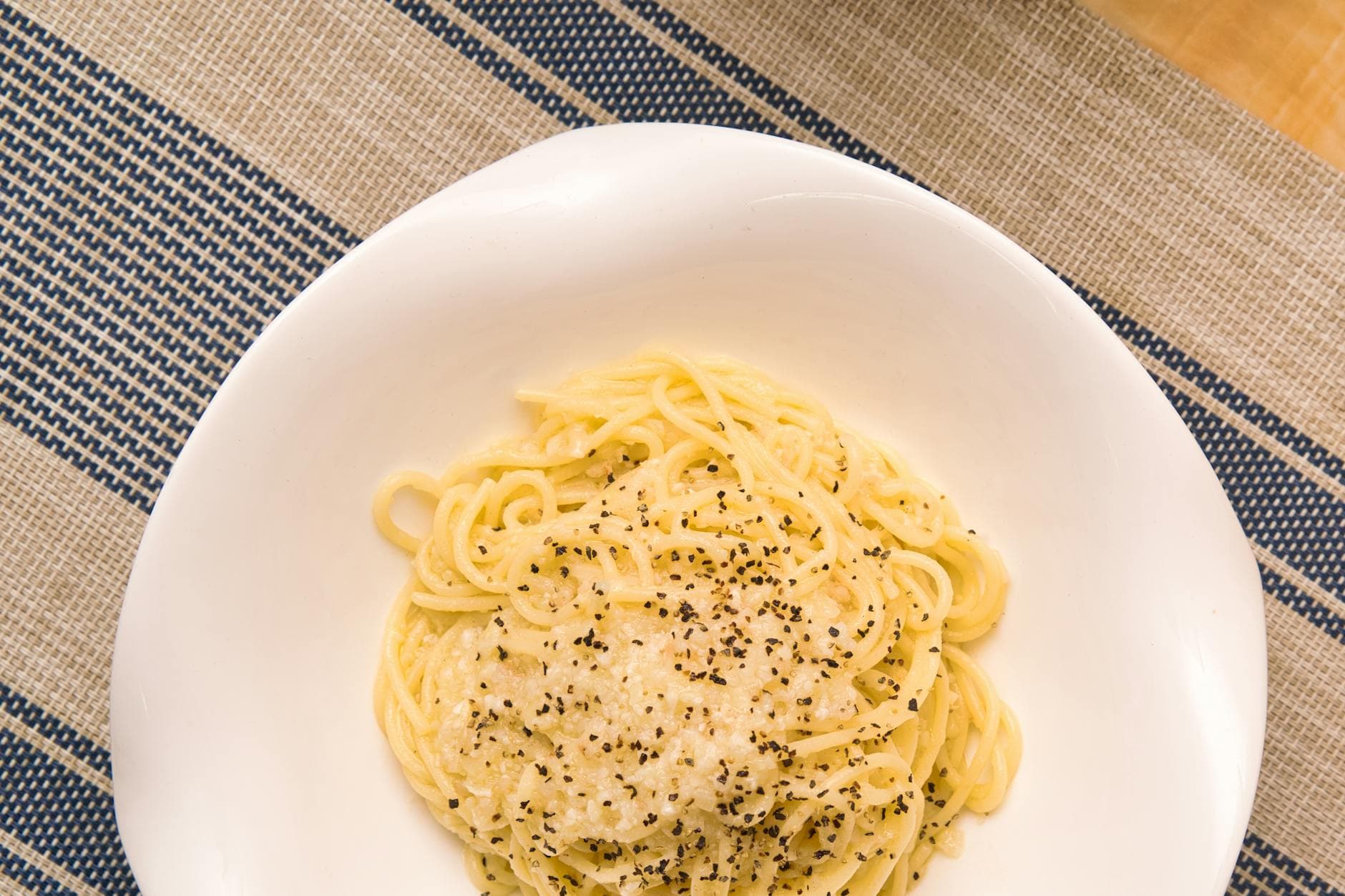 Top view of tasty pasta with melted cheese topped with ground black pepper served in white plate on table with colorful tablecloth