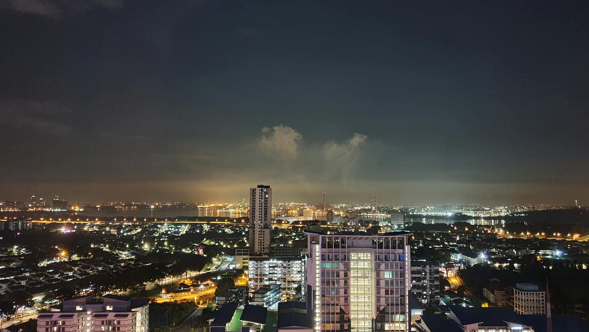 A vibrant night view of the Johor Bahru skyline with illuminated city lights and clear sky.