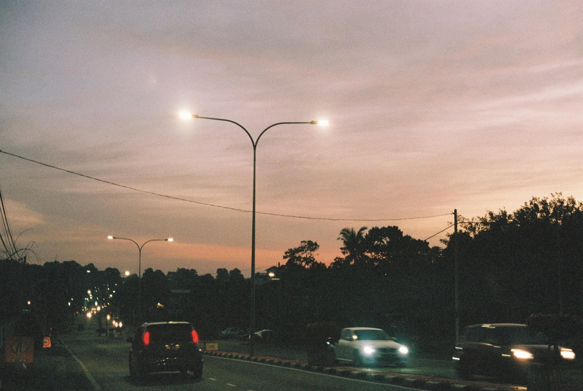 A twilight scene of cars on a street in Kluang, Johor, Malaysia, with street lamps glowing.