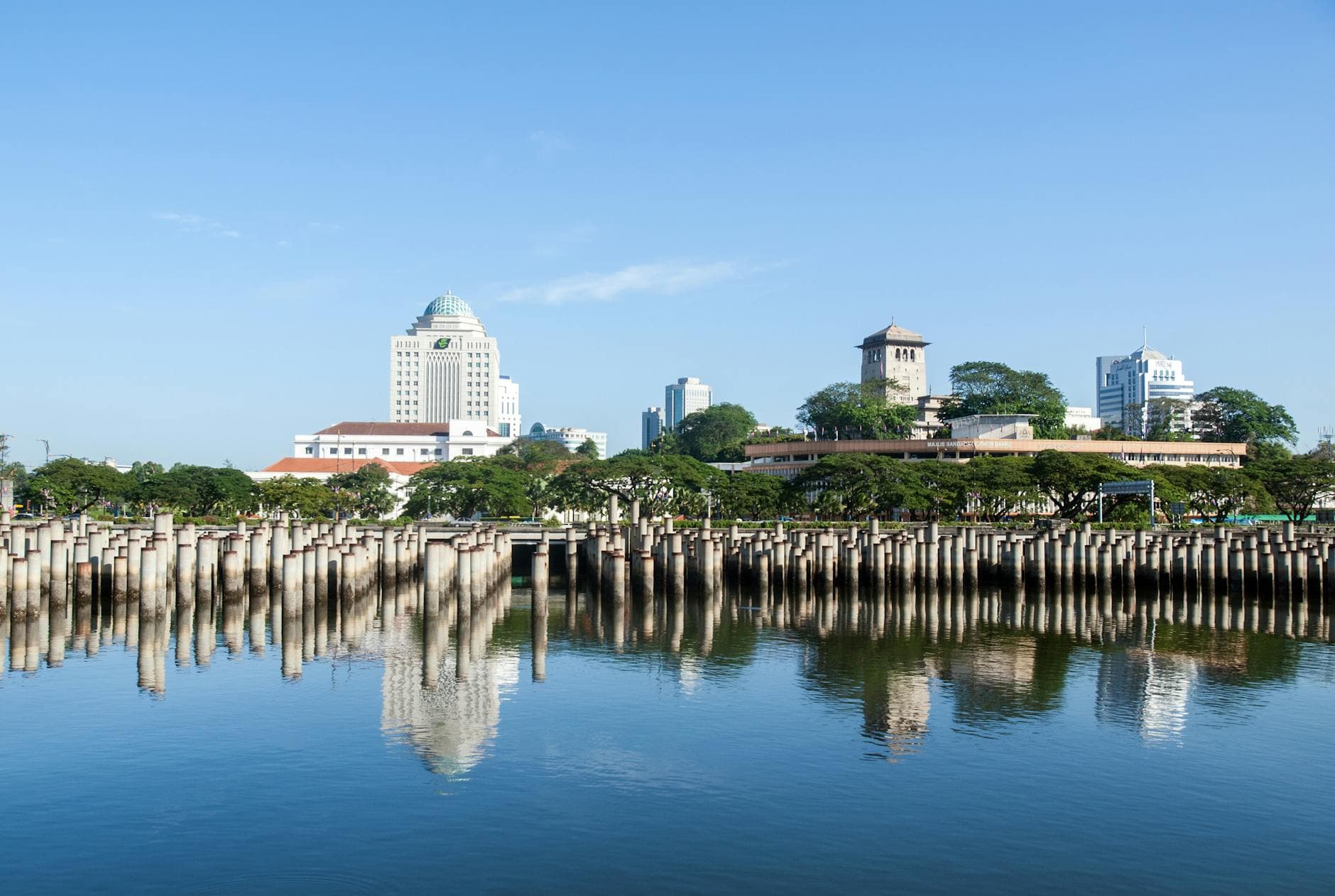 Beautiful view of Johor Bahru skyline reflecting on calm water on a sunny day.