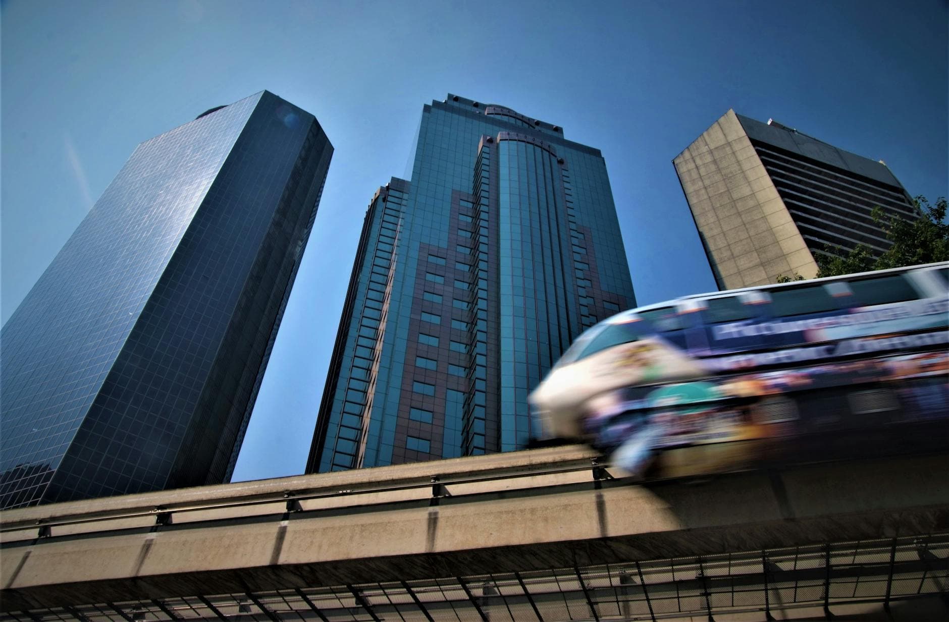 Skyscrapers in Kuala Lumpur with a monorail train in motion against a clear blue sky.