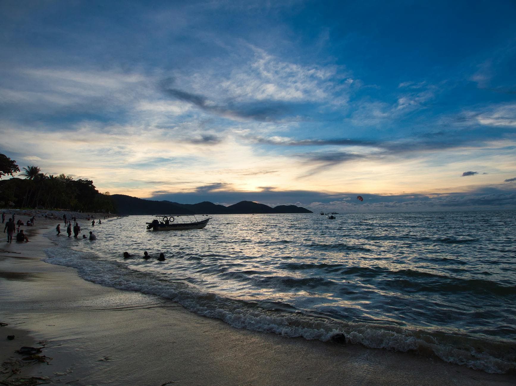 A serene sunset view over Batu Ferringhi Beach in Penang, Malaysia, with silhouettes and waves.