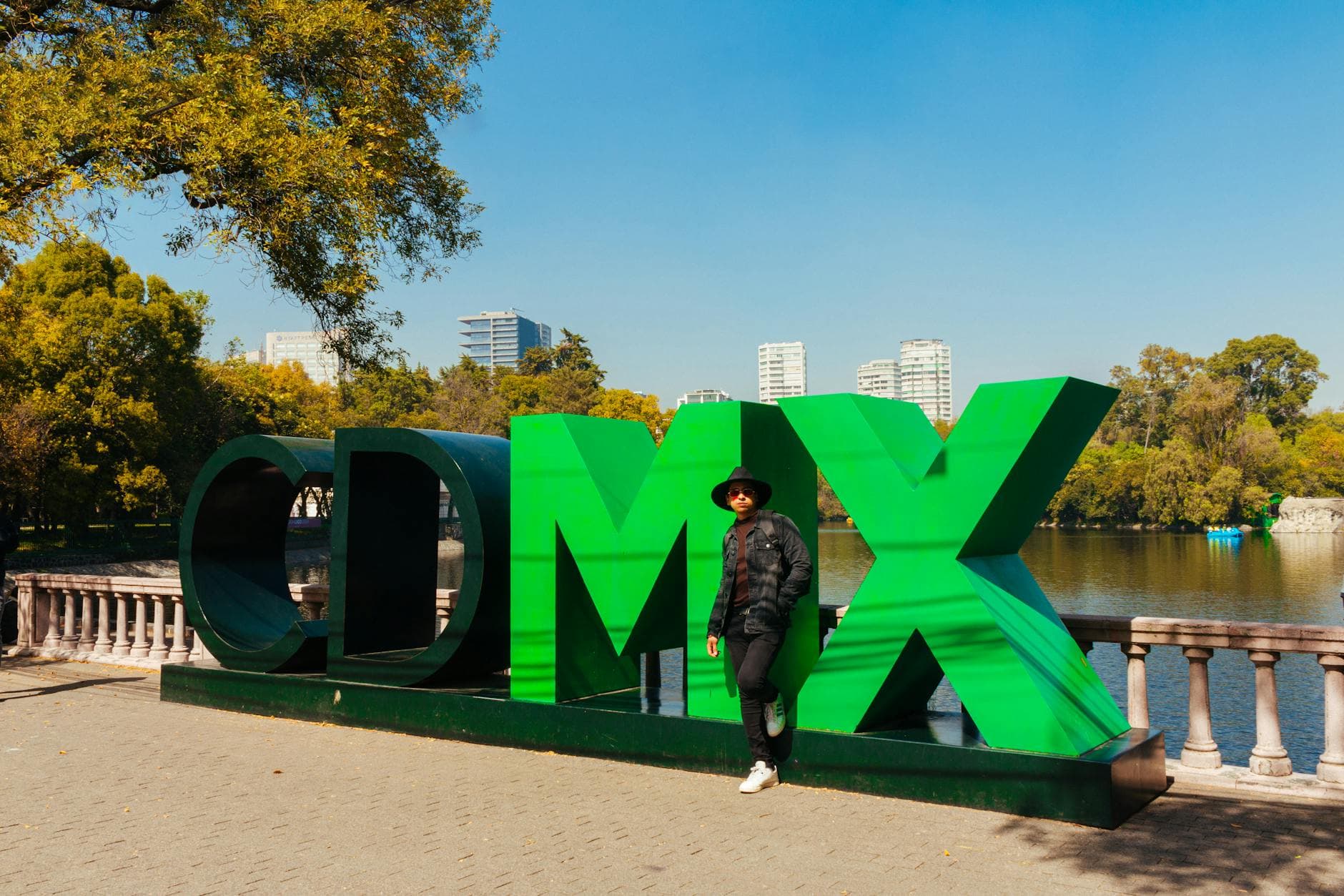 Man standing by the iconic green CDMX sign in a sunny urban park in Mexico City.