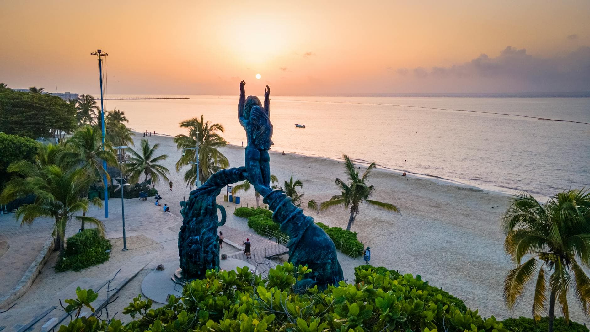 Stunning sunset view at Portal Maya sculpture, Playa del Carmen beachside with palm trees and serene sea.
