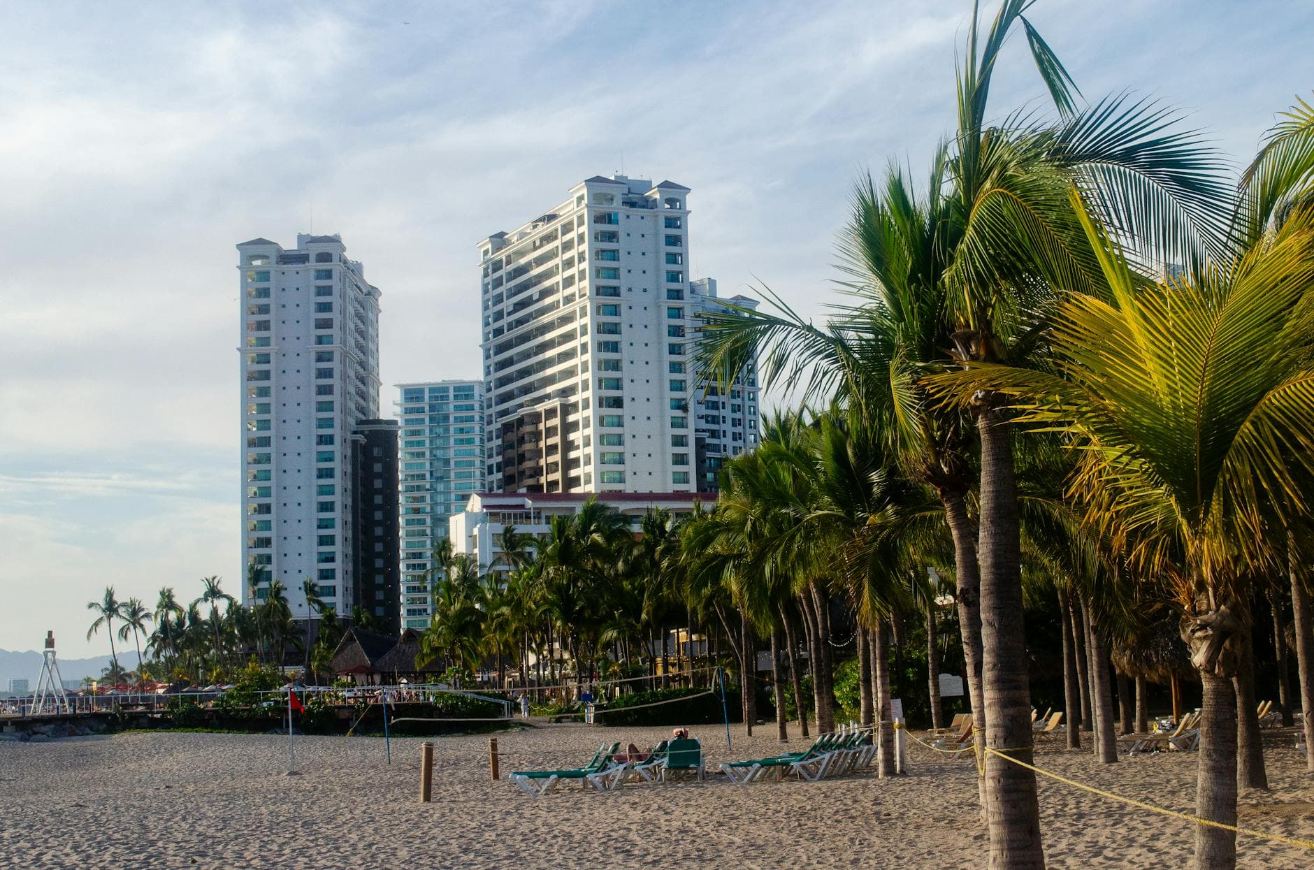 Modern beachfront skyscrapers and palm trees in Puerto Vallarta, Mexico, with sandy shores and clear skies.