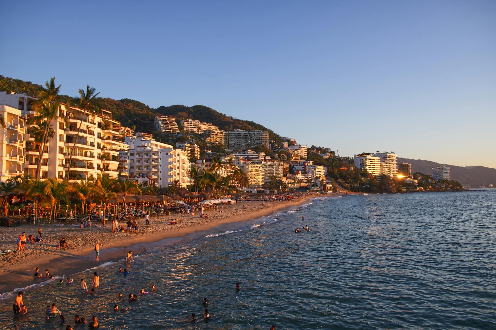 Explore the vibrant coastline of Puerto Vallarta, Mexico with bustling beach activity and scenic resorts at sunset.