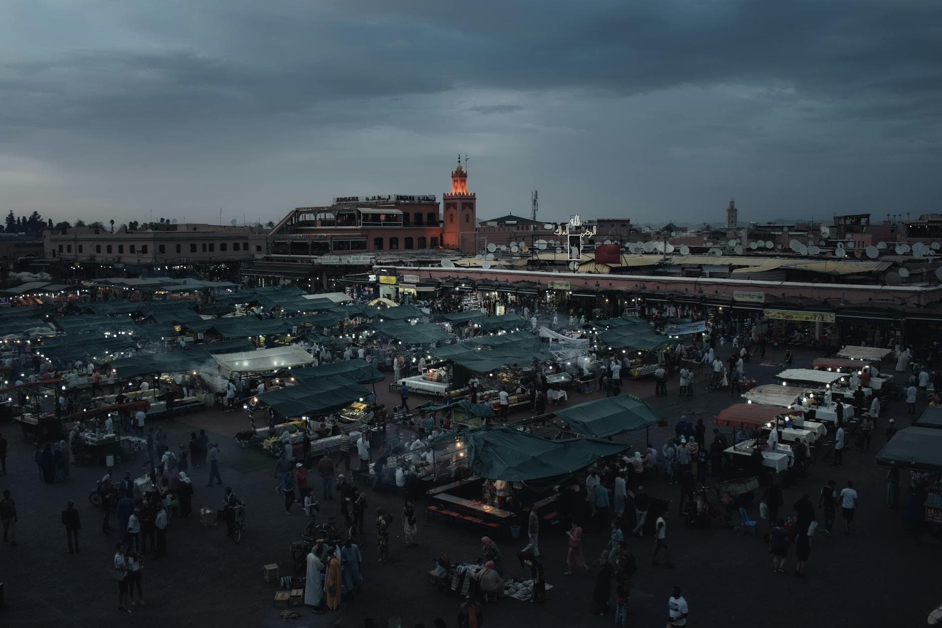A vibrant night market in Marrakech bustling with people under a dusky sky.