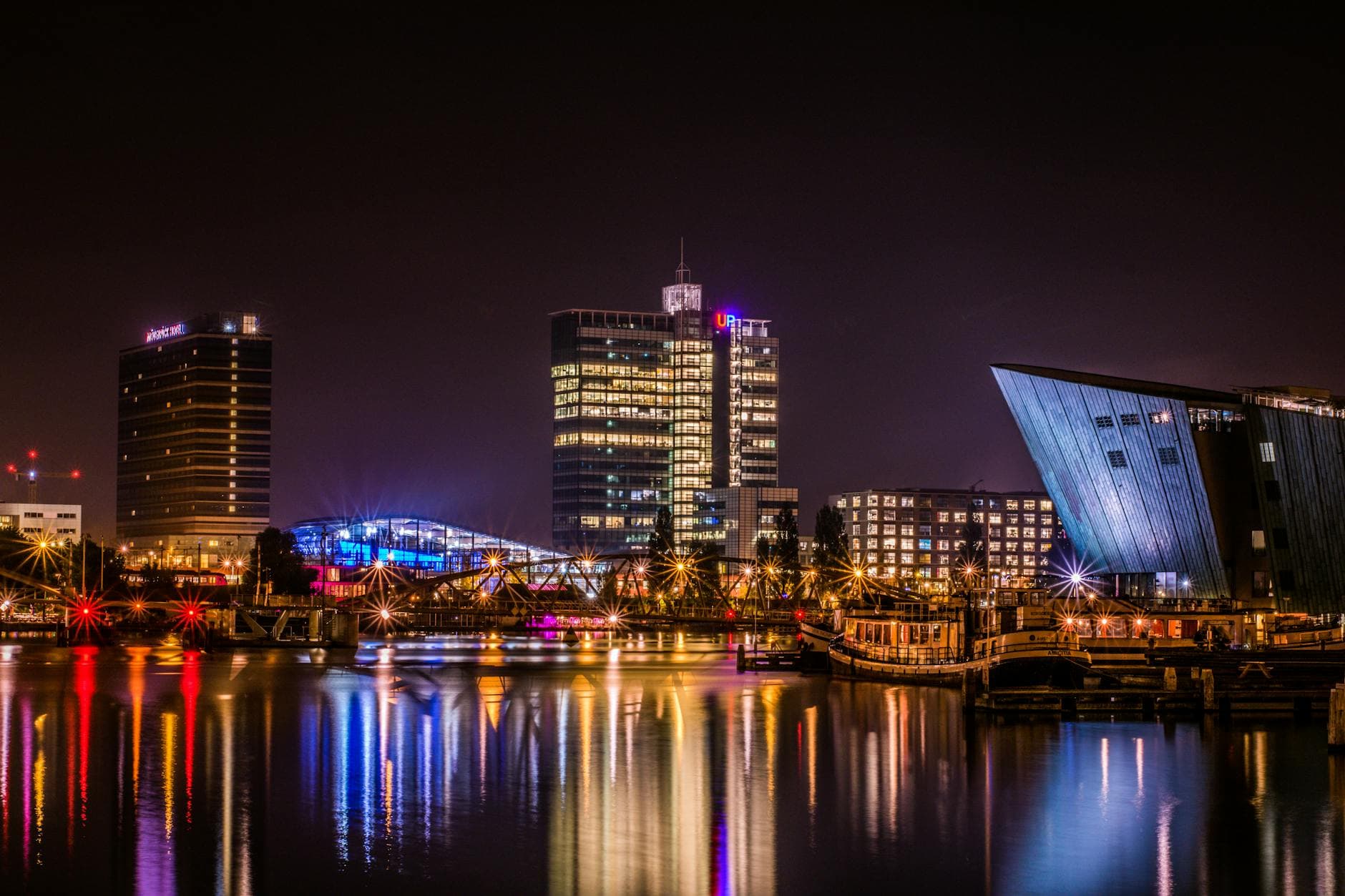 Reflective night view of Amsterdam's modern skyline by the water.