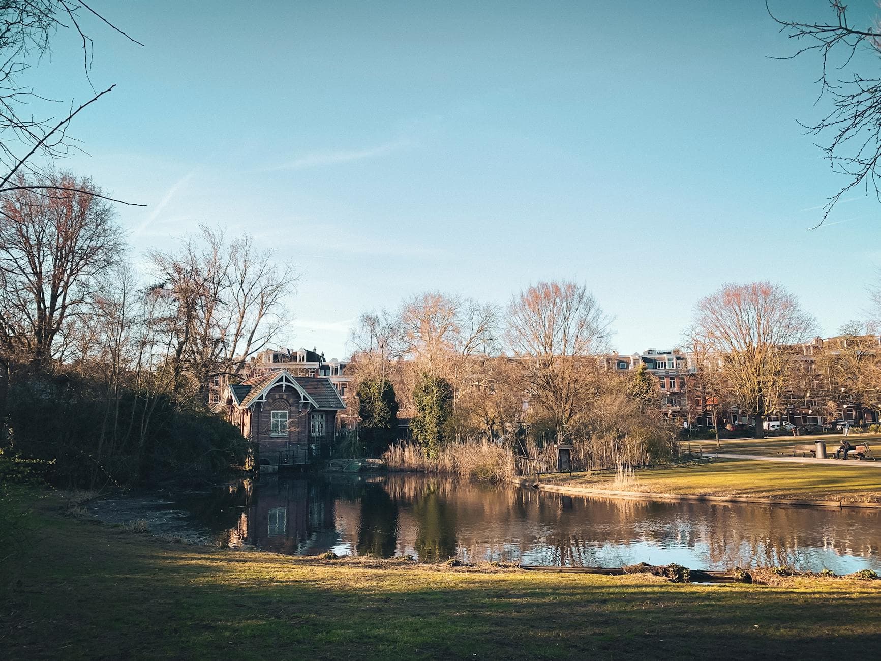 Tranquil park scene in Amsterdam with a pond and charming architecture.
