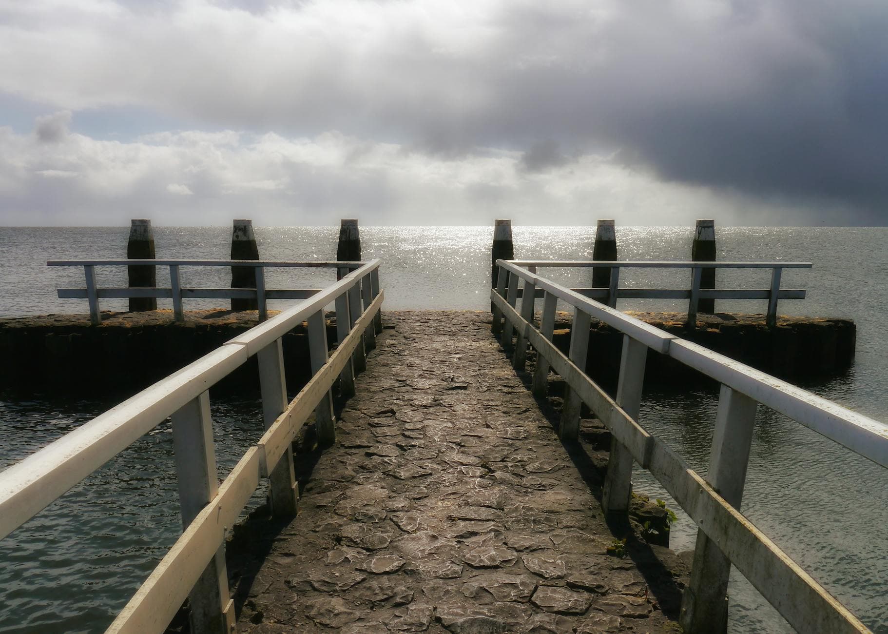 Peaceful pier at Wierum, Friesland, overlooking the shimmering Wadden Sea under a cloudy sky.