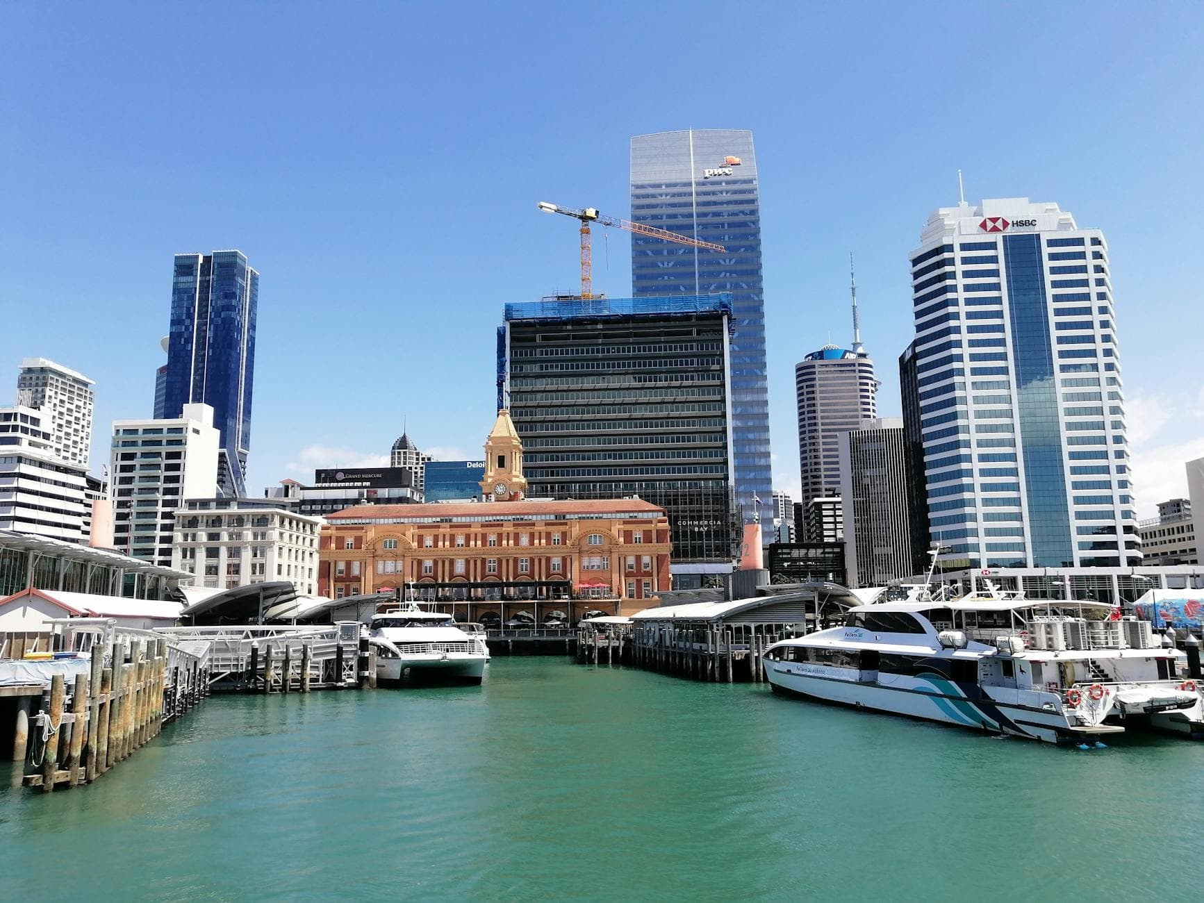 Vibrant Auckland cityscape featuring waterfront, skyscrapers, and yachts under a clear blue sky.