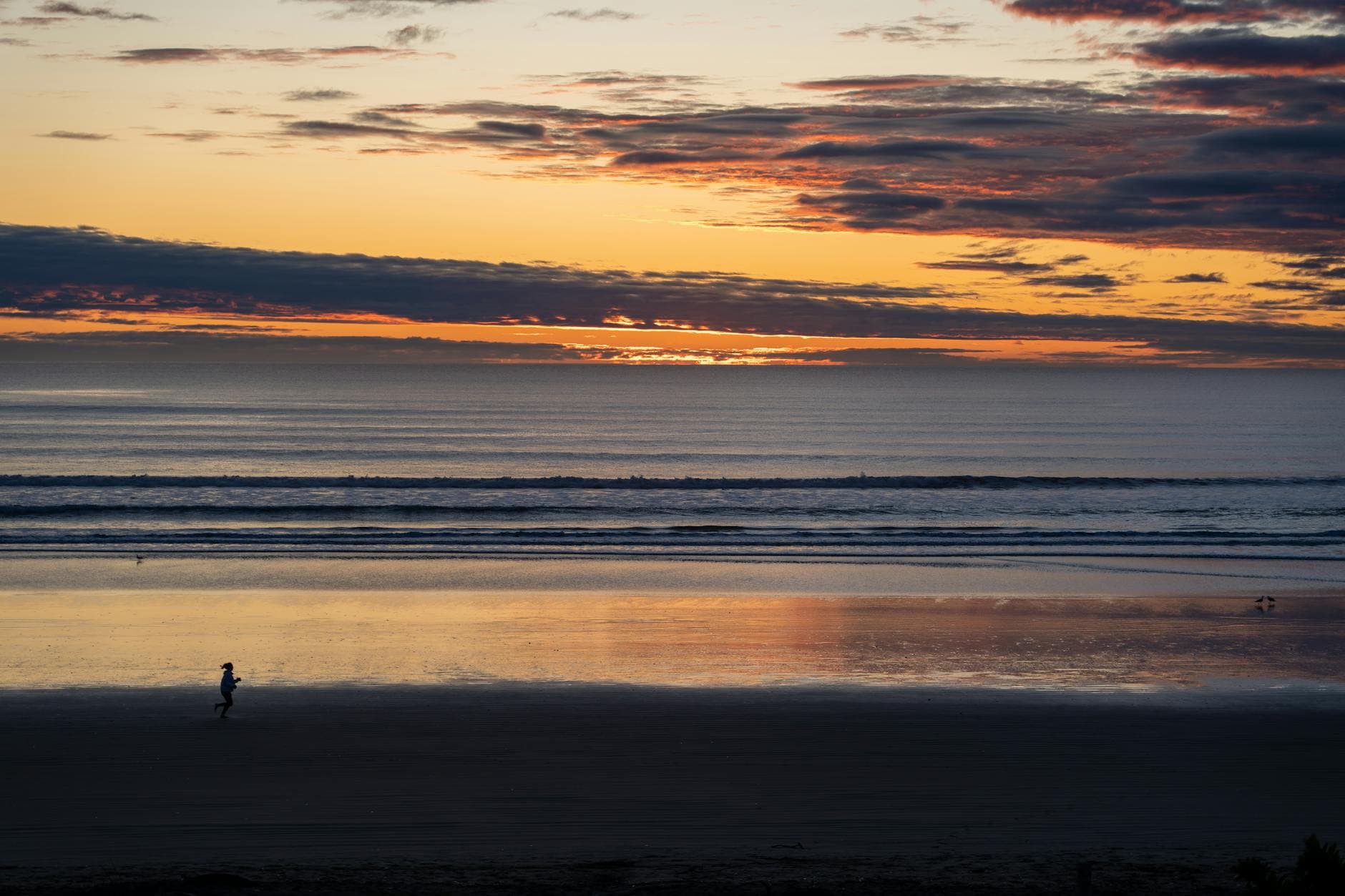 A serene view of a person running along a tranquil beach at sunset in Christchurch, New Zealand.