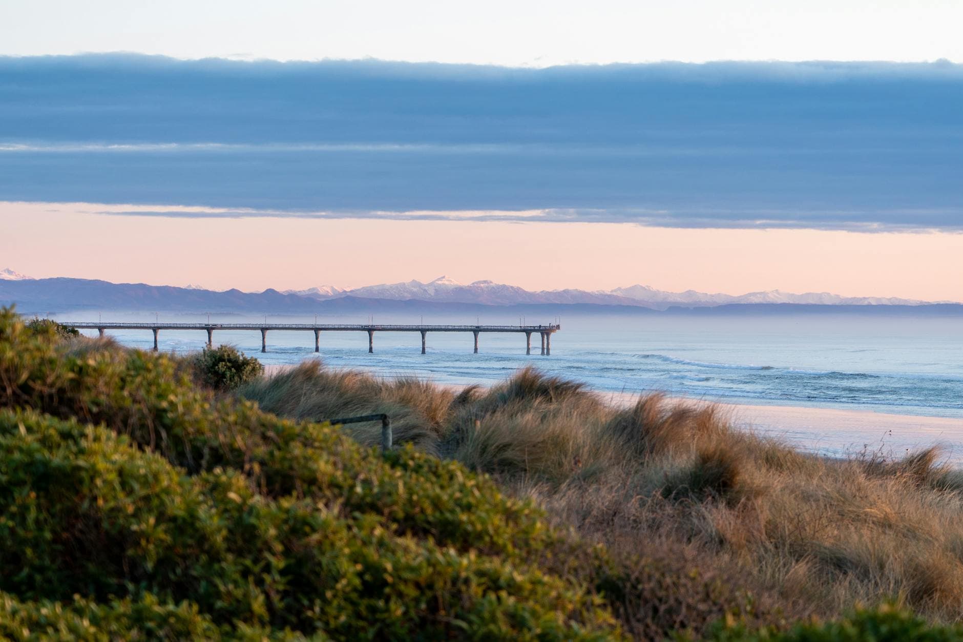 Stunning sunset view over Christchurch pier with coastal vegetation and serene waves.