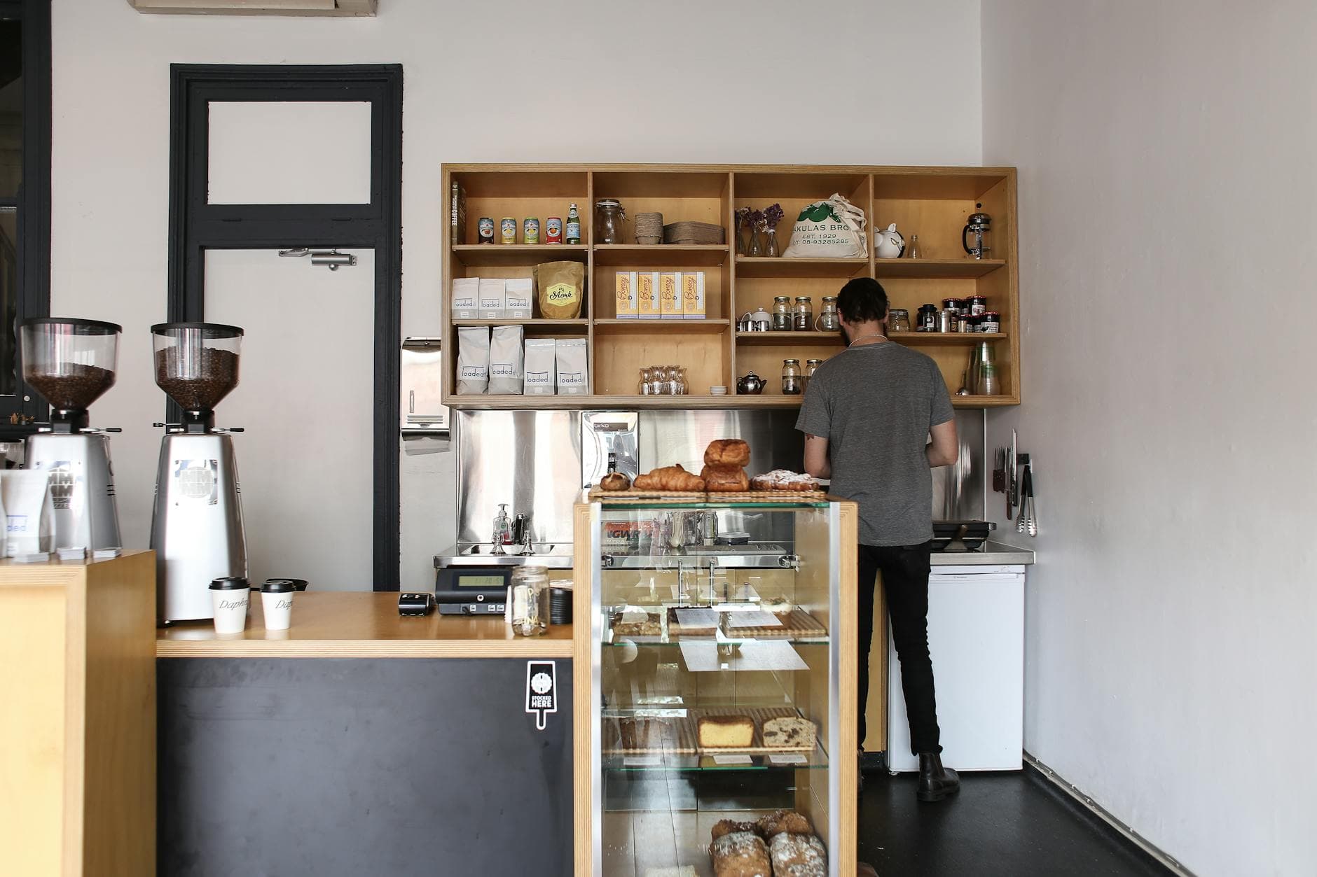 Barista working in a modern café with well-organized shelves and coffee equipment.