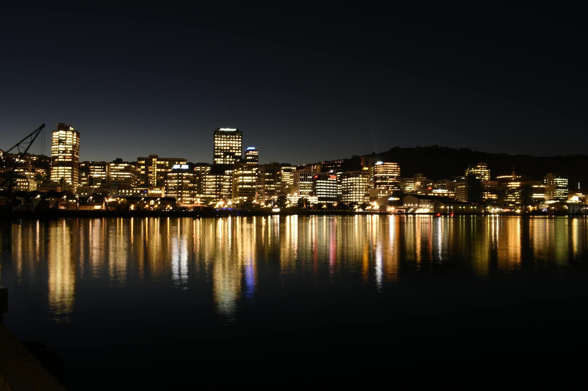 A stunning view of Wellington city illuminated at night with reflections on water, showcasing urban architecture.