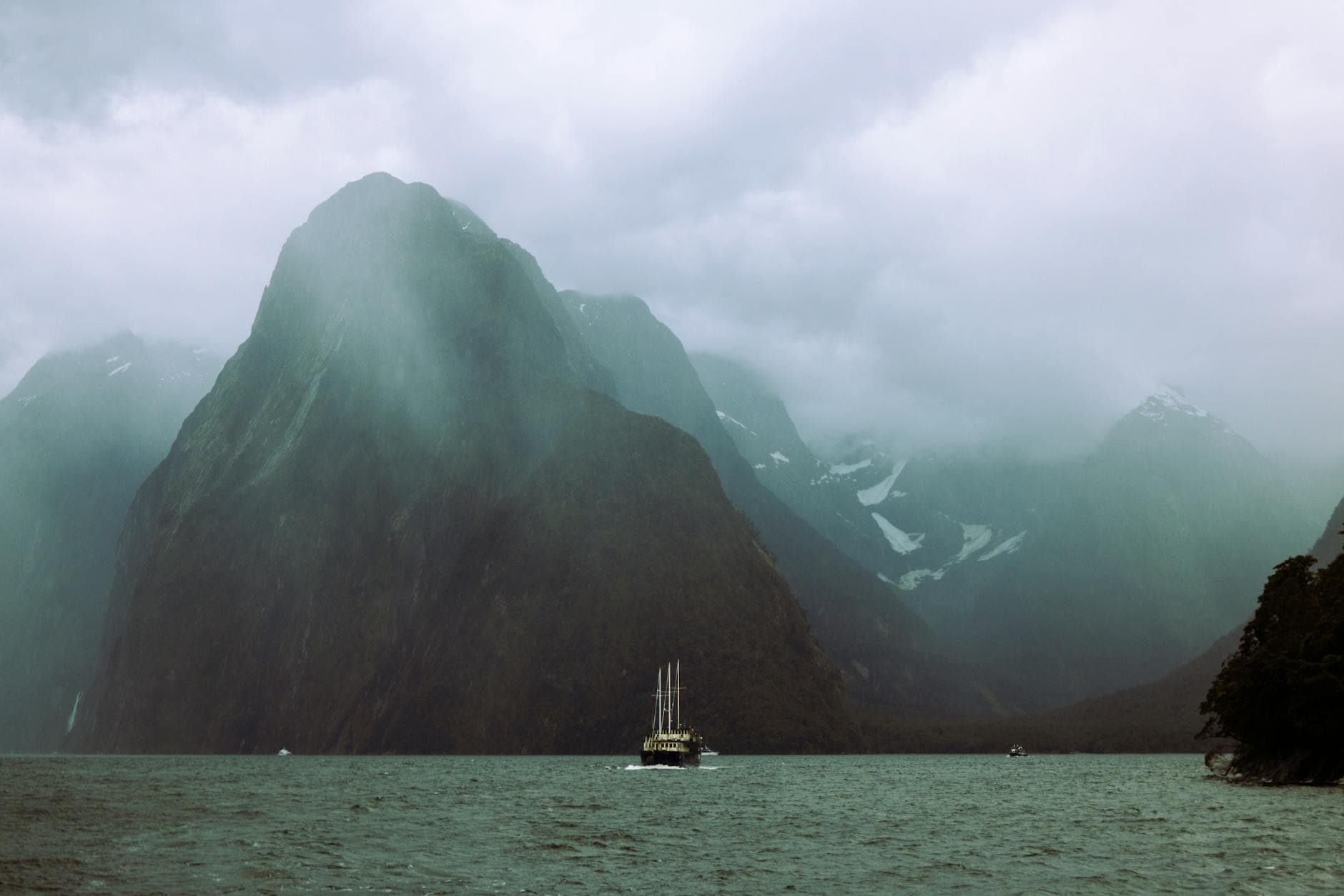A sailboat navigating the dramatic and cloudy landscape of Milford Sound.