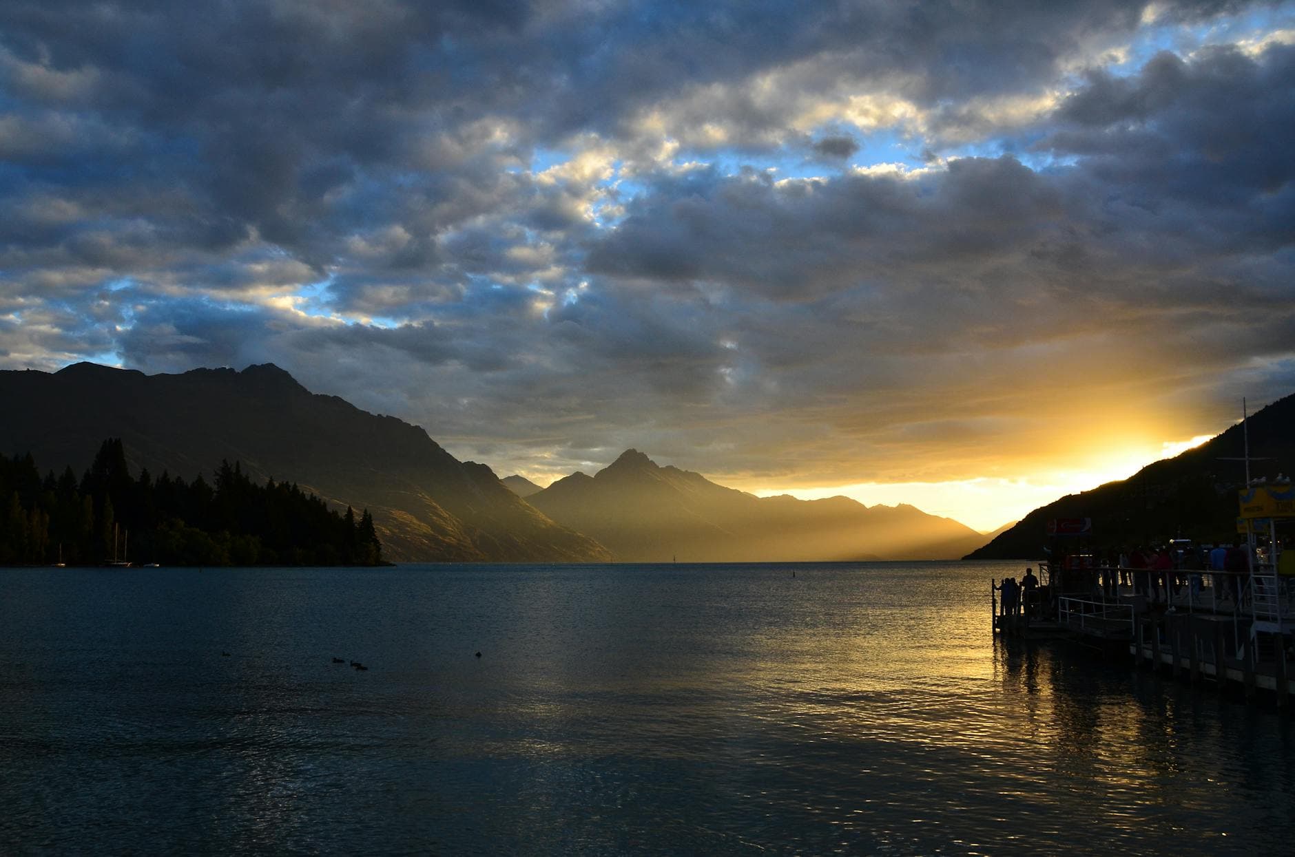 Dramatic sunset over Lake Wakatipu in Queenstown, highlighting mountain silhouettes and vibrant skies.