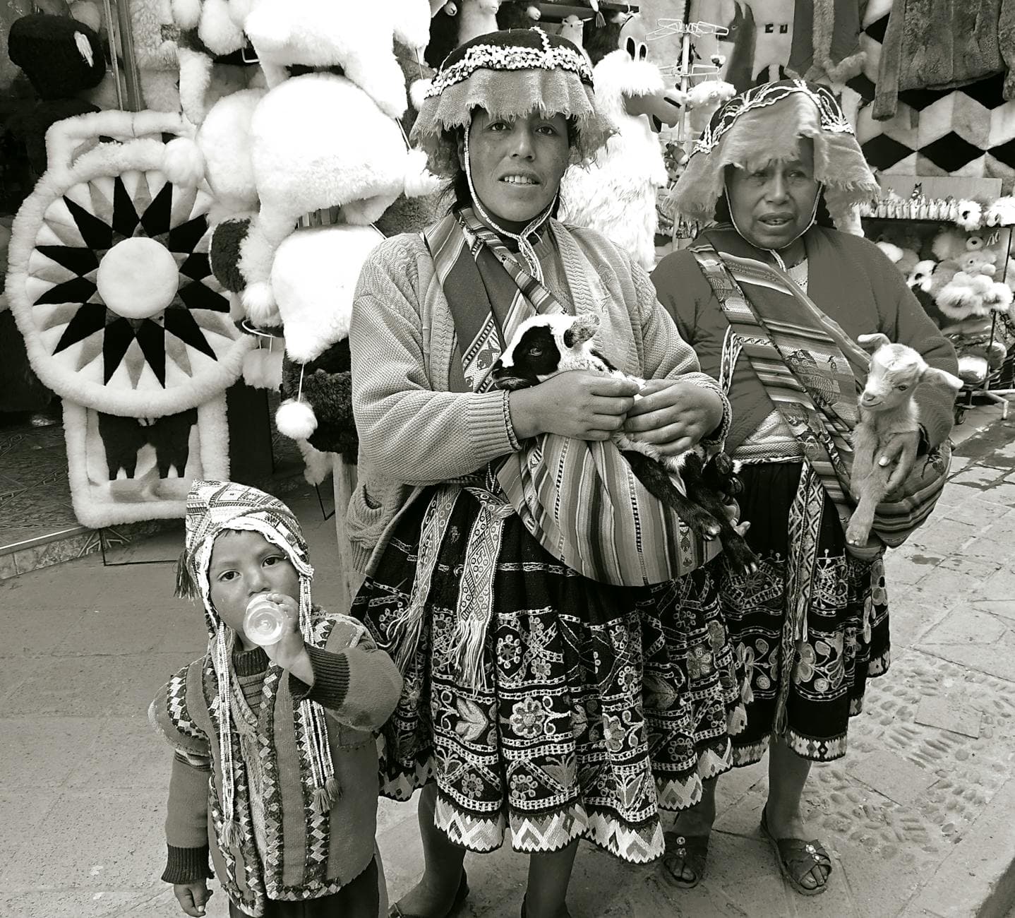 Black and white photo of an Andean family in traditional attire, holding lambs in a market setting.