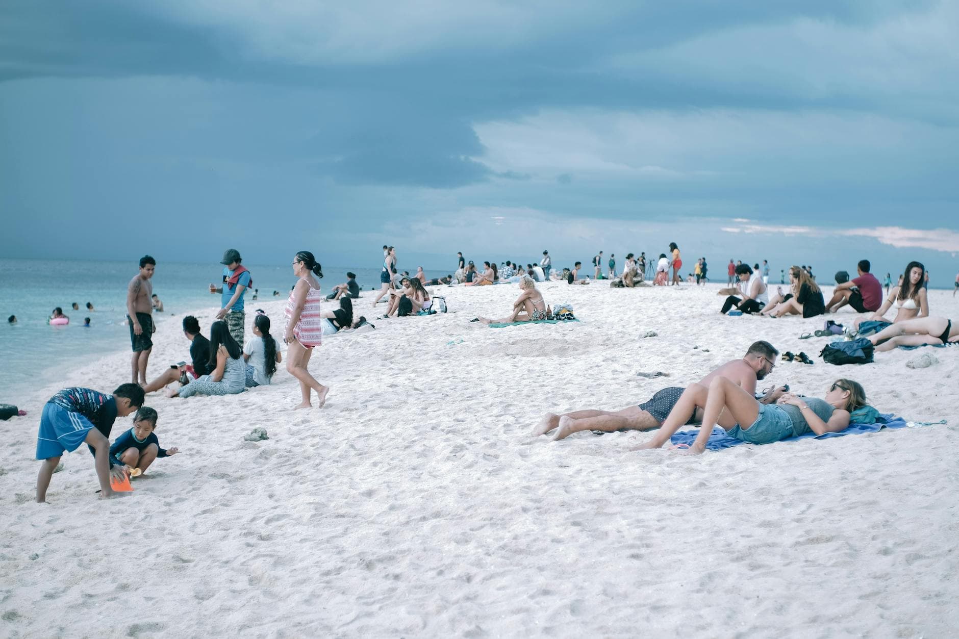 Vacationers enjoy the white sandy beach in Cebu City, Philippines under a cloudy sky.
