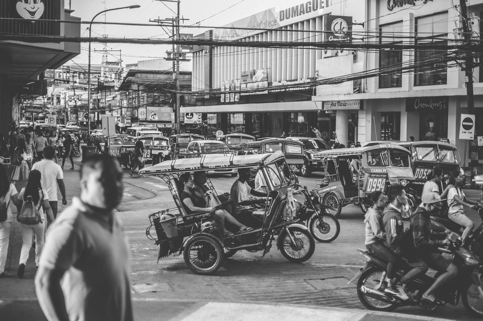 Bustling street in Dumaguete City with motorbikes and tricycles navigating traffic in black and white.